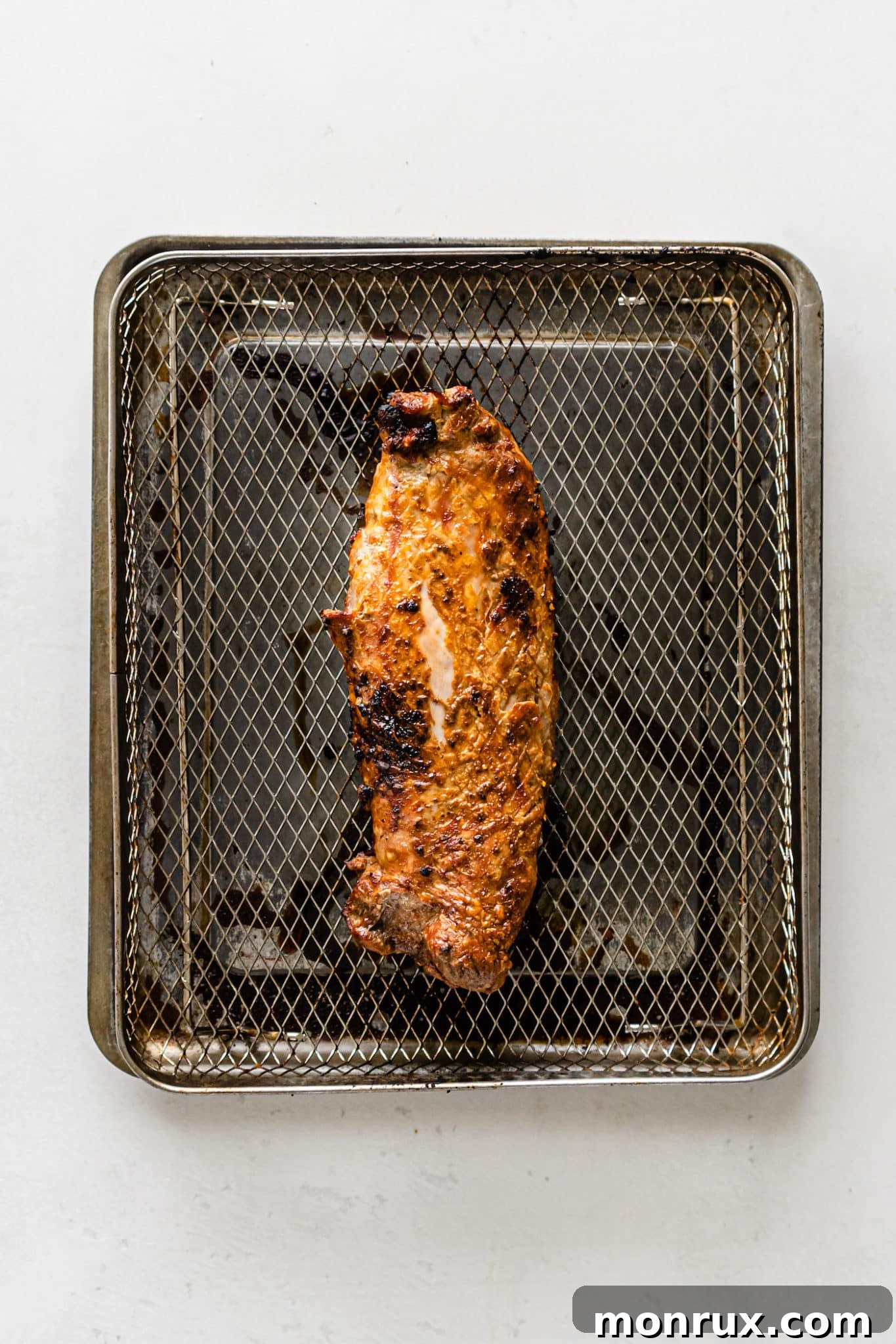 A perfectly cooked pork loin roast resting inside an air fryer basket after its initial cooking phase.