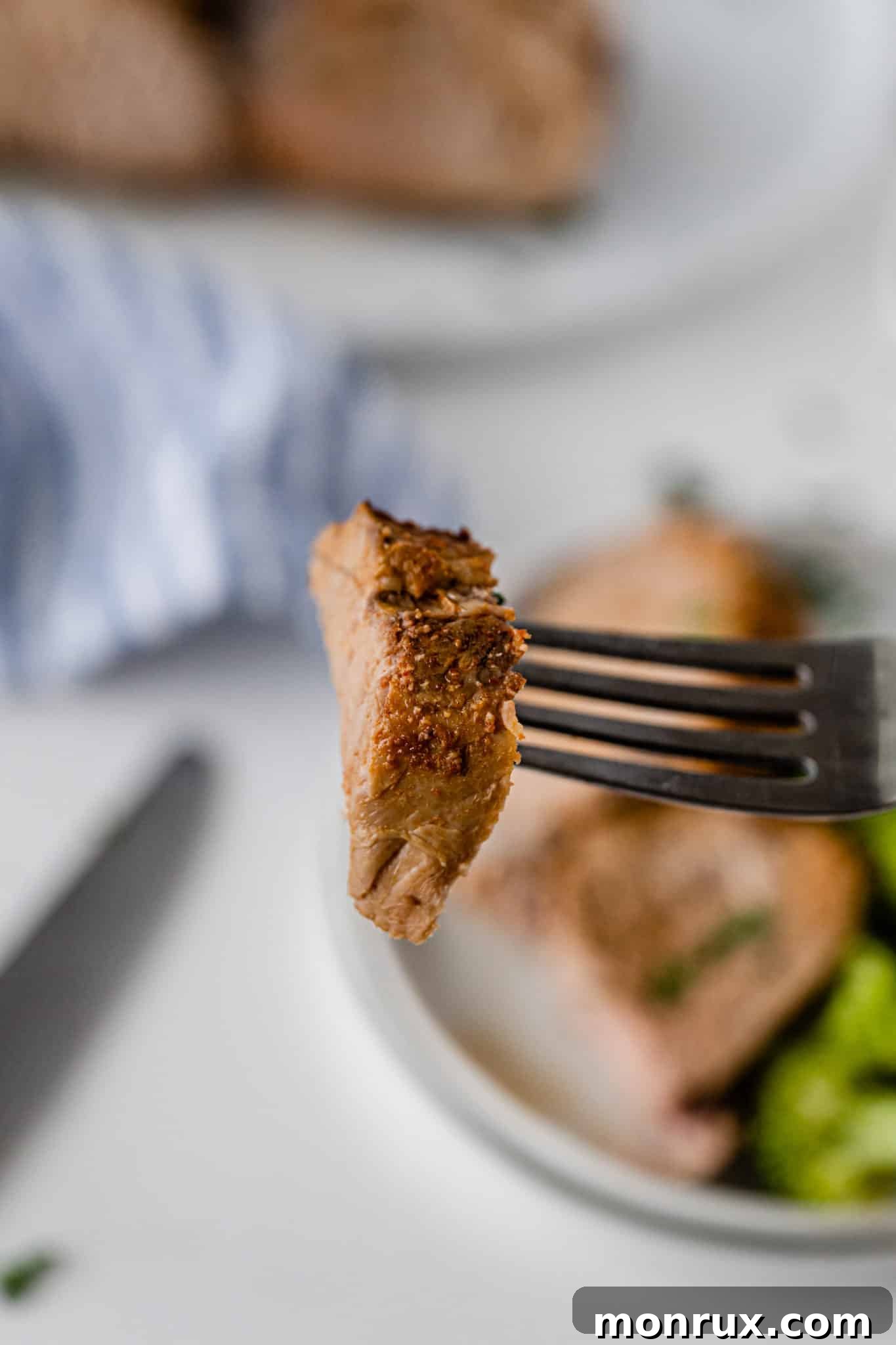 A close-up shot of a tender, cooked bite of pork loin on a fork.