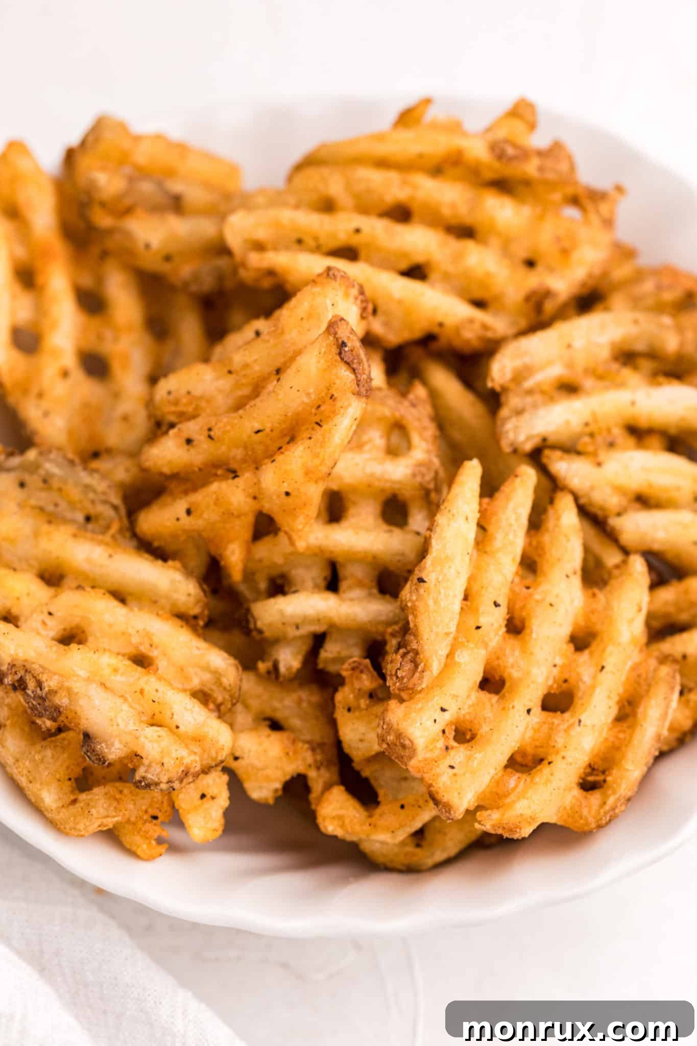 A serving of crispy, golden waffle fries presented in a clean white bowl, ready to be enjoyed.