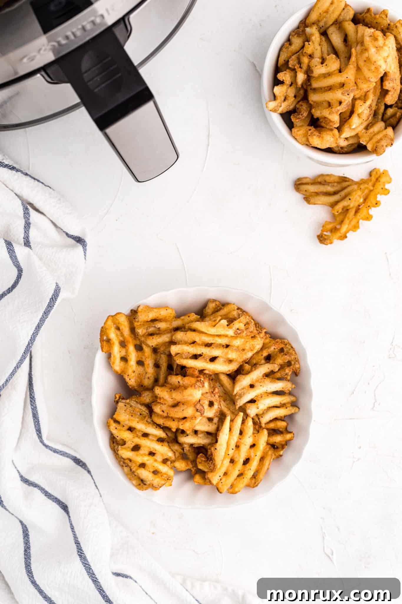 Two white bowls filled with golden, perfectly cooked waffle fries, ready to be served and enjoyed.