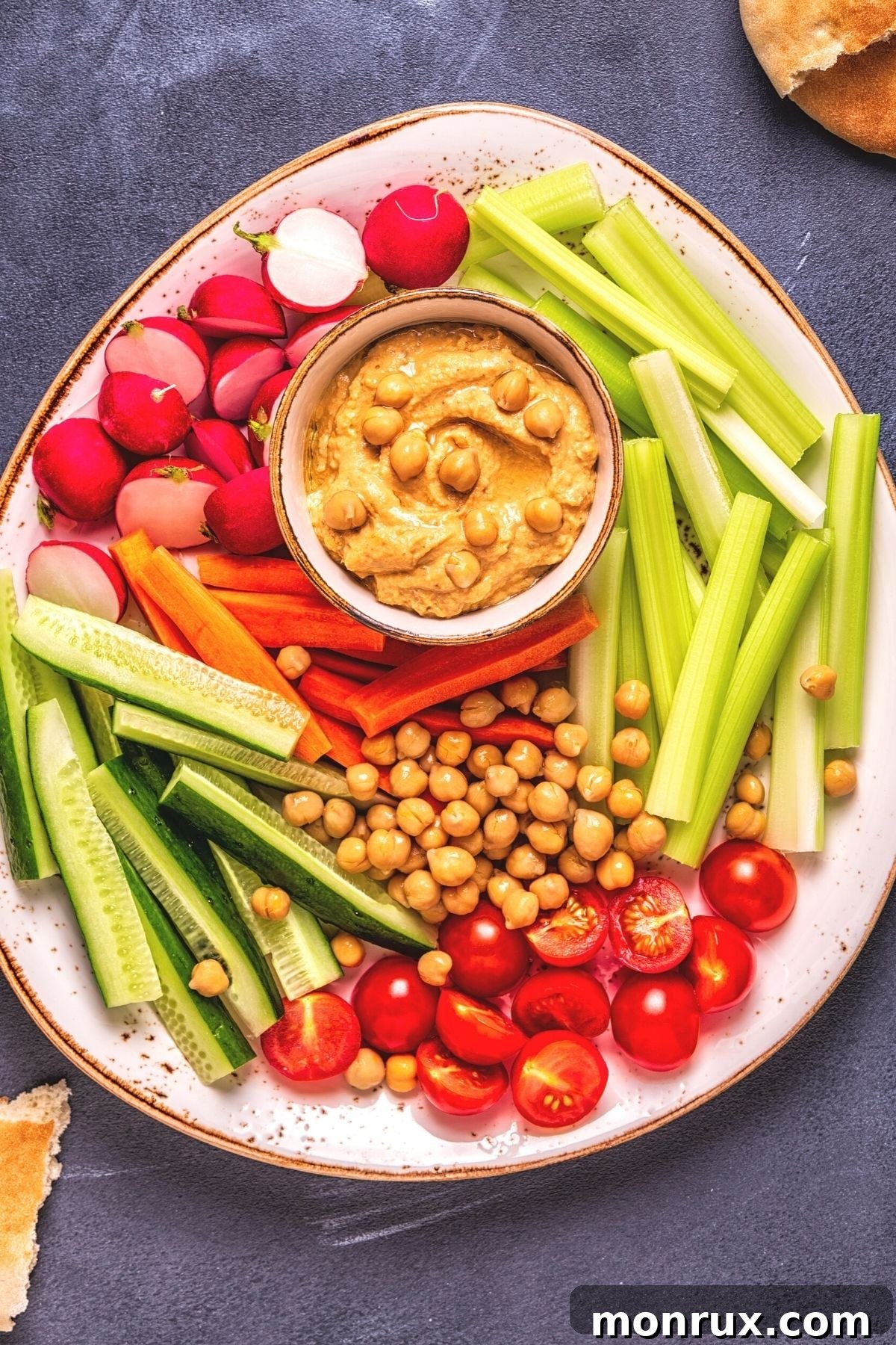 A vibrant platter featuring homemade hummus surrounded by an assortment of fresh, colorful vegetables like carrots, celery, and bell peppers.