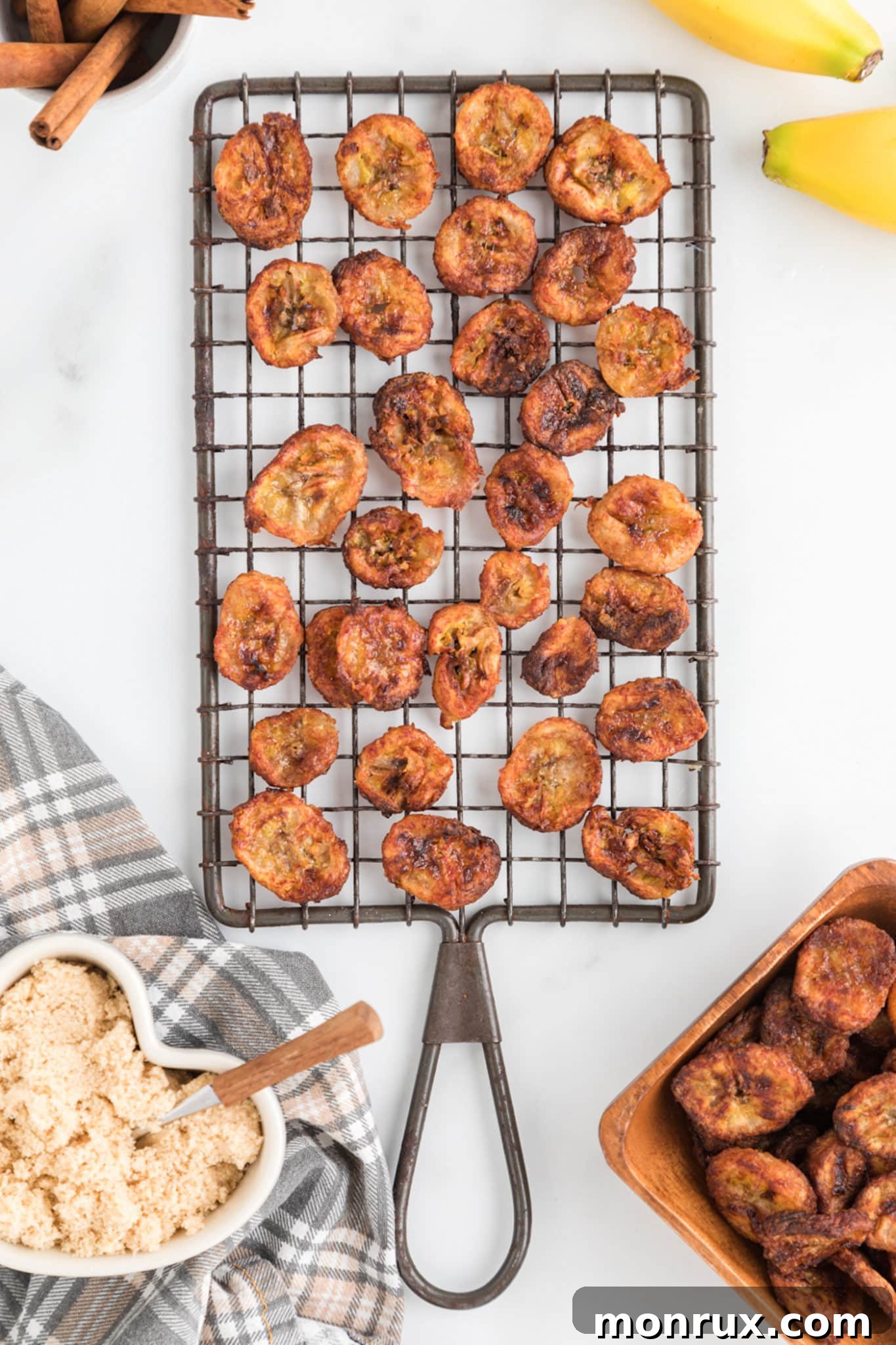 Air fryer cinnamon banana chips neatly arranged on a cooling rack, set against a pristine white kitchen counter background.