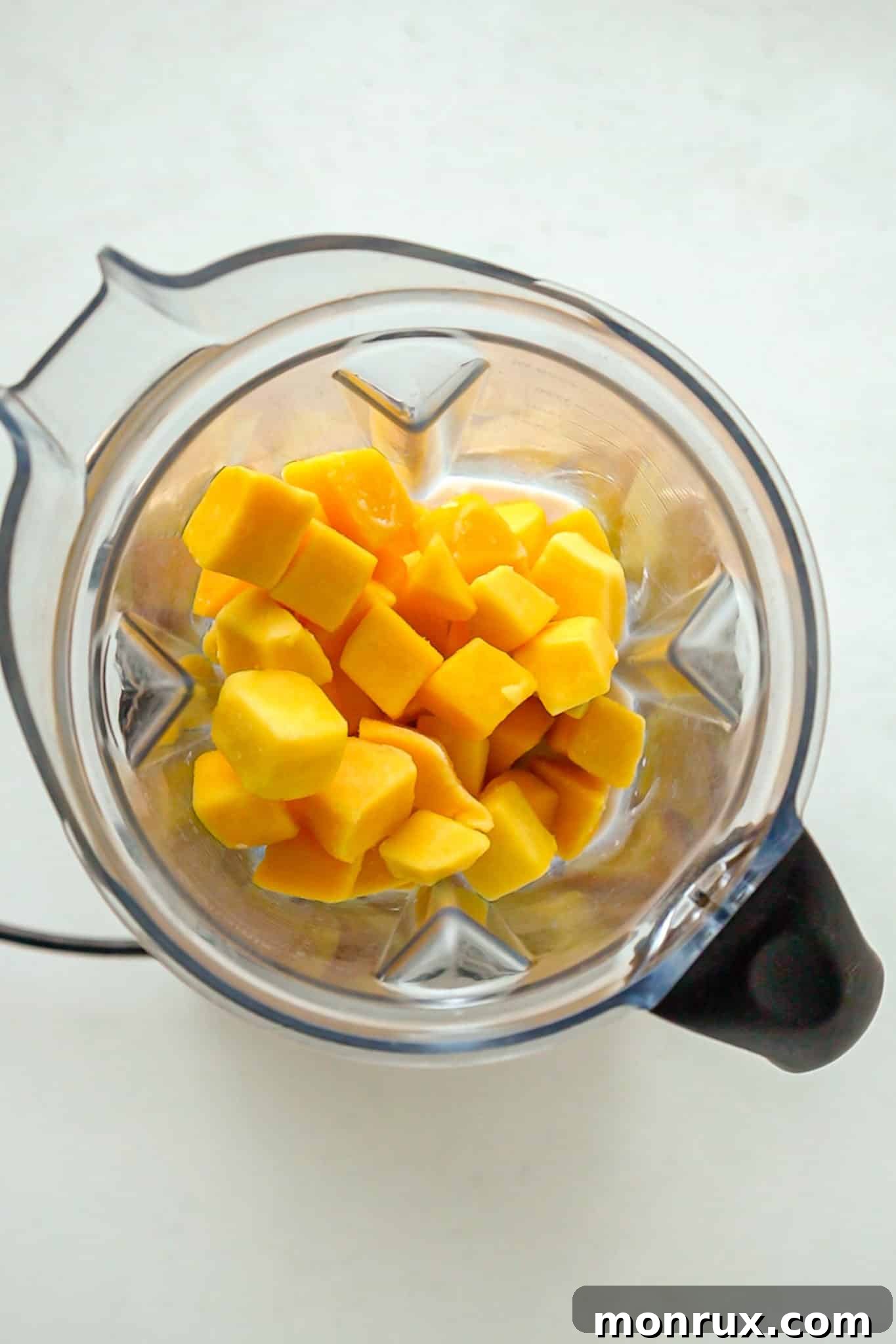 Frozen mango chunks and liquid ingredients being added to a Vitamix blender container.