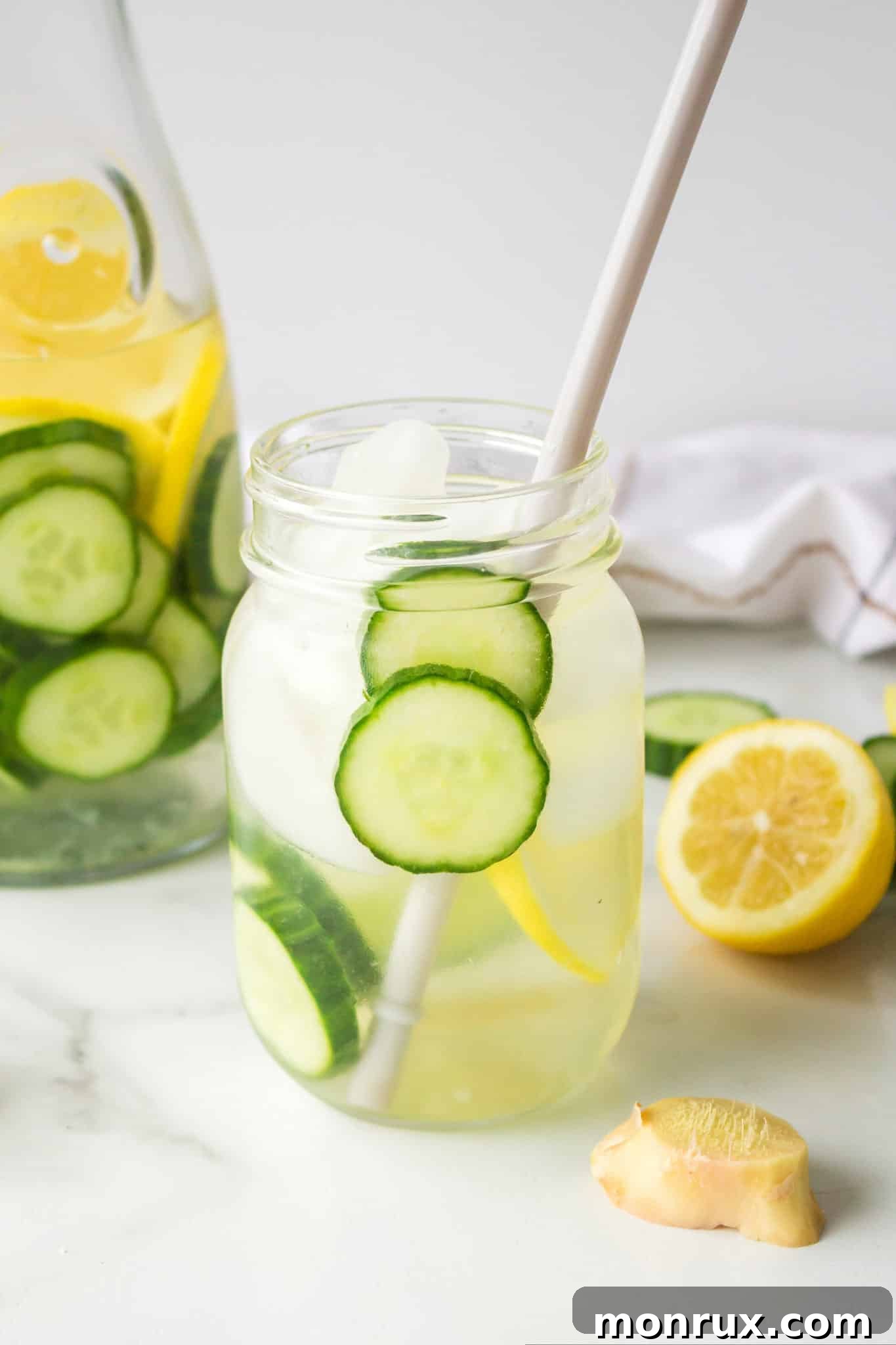 cucumber ginger lemon water in jar with ice cubes and paper straw.