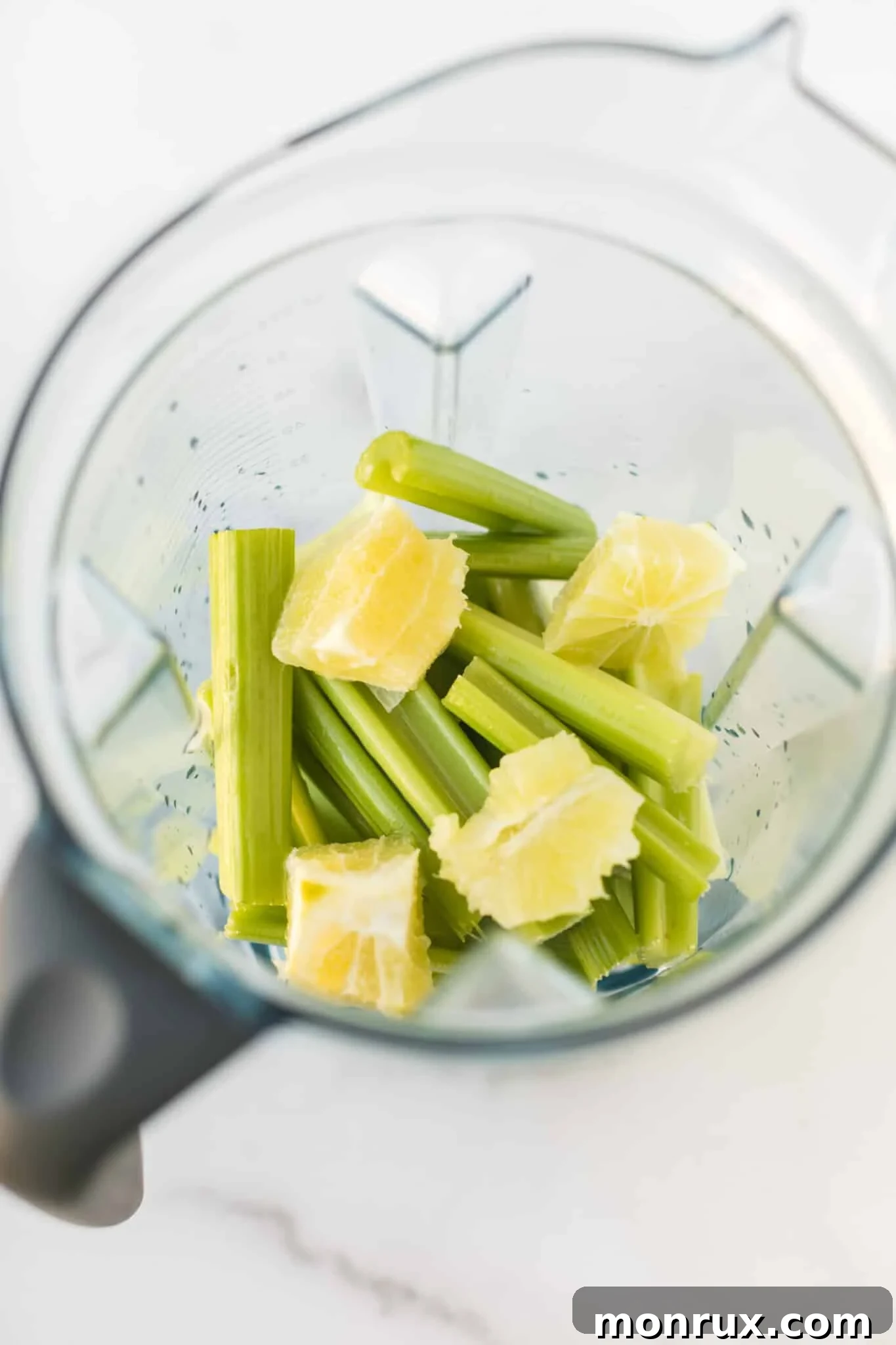 Freshly cut cucumber, celery, ginger, apple, lemon, and spinach are neatly arranged in a Vitamix blender, ready for juicing.