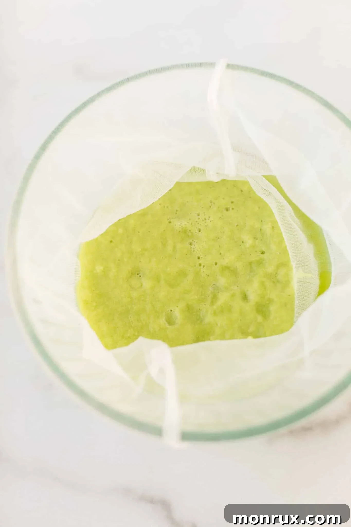 The process of straining blended green juice through a nut milk bag, separating the liquid from the pulp.