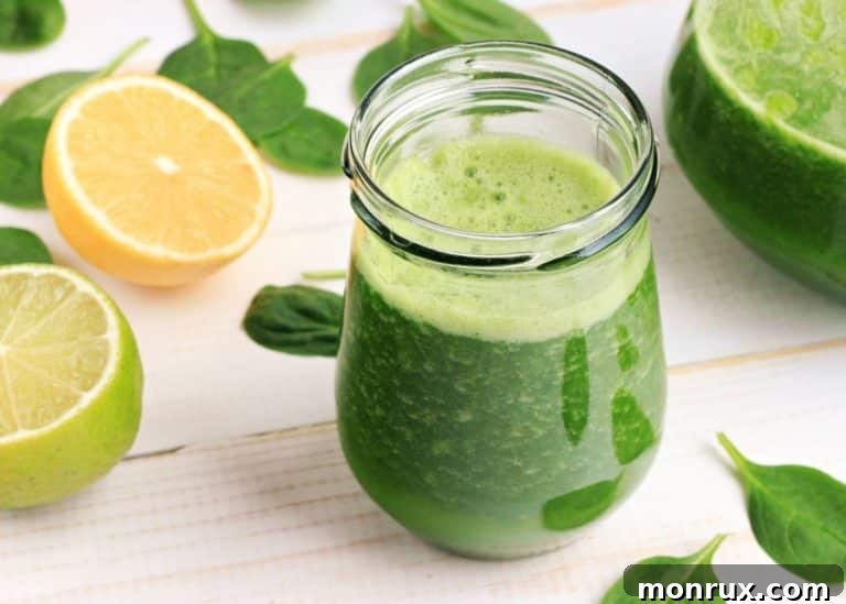 A glass of vibrant green juice, made using a Vitamix blender, presented with fresh ingredients like cucumber and spinach.