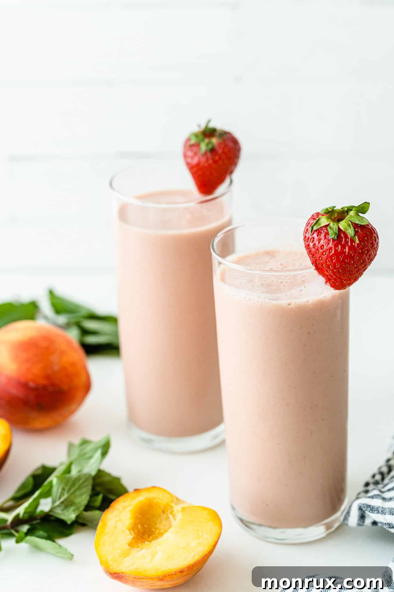 Two glasses of vibrant strawberry peach smoothies, garnished with fresh strawberries, embodying summer refreshment.
