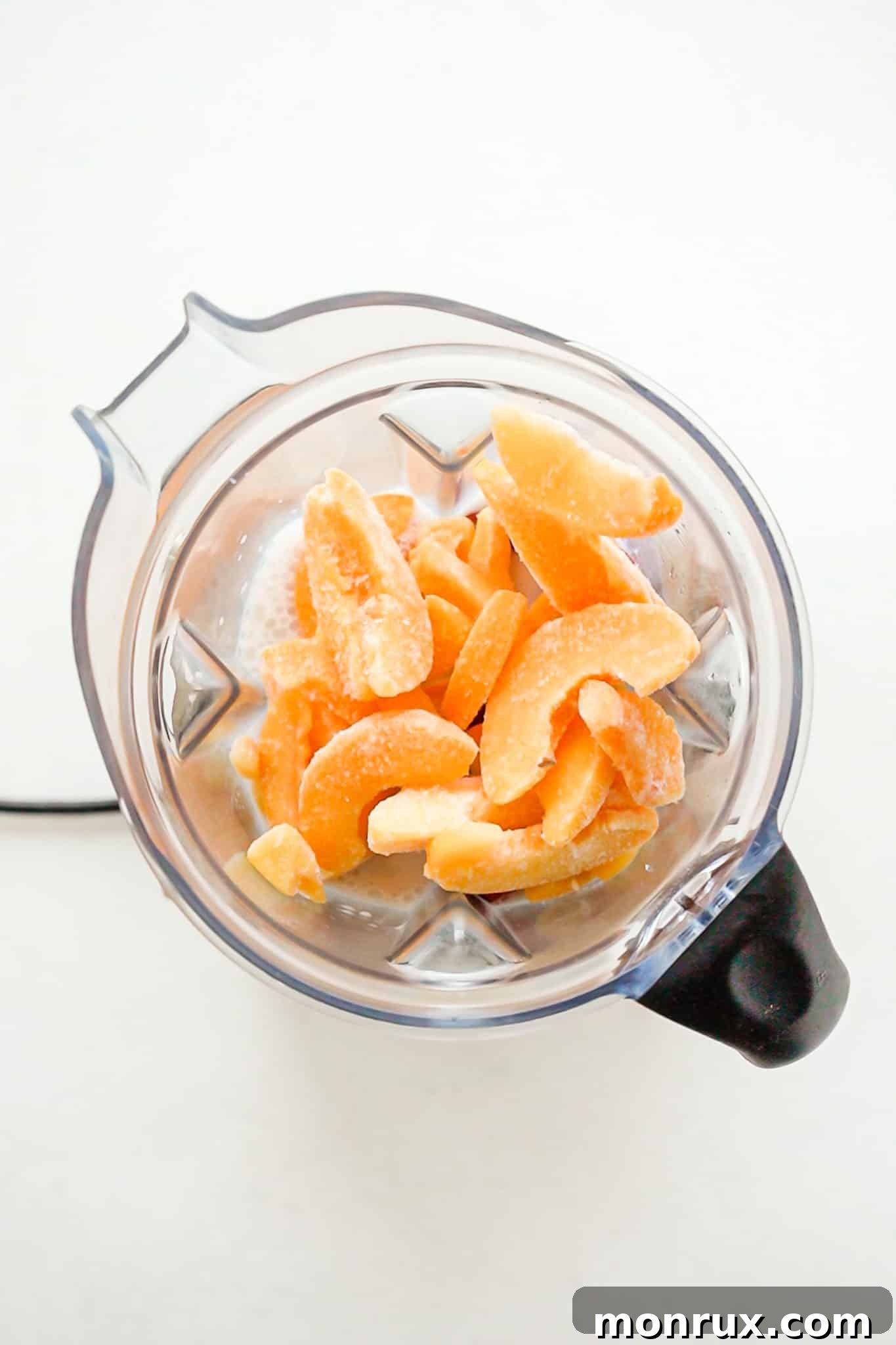 Frozen peaches being added to a high-speed blender, ready for blending.