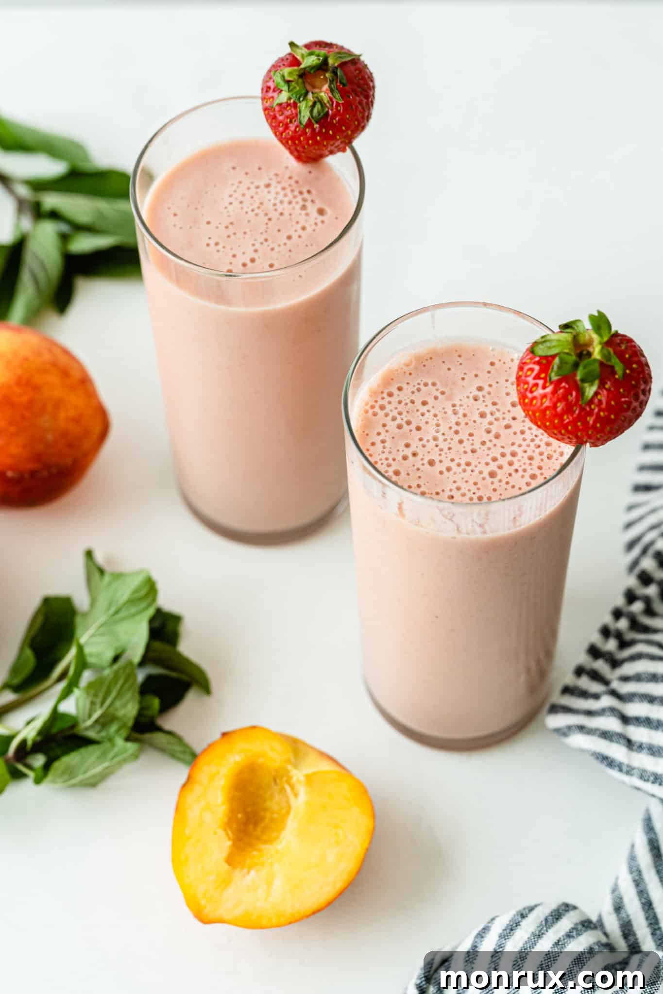 Two glasses of strawberry peach smoothies, garnished with fresh fruit, presented beautifully for enjoyment.