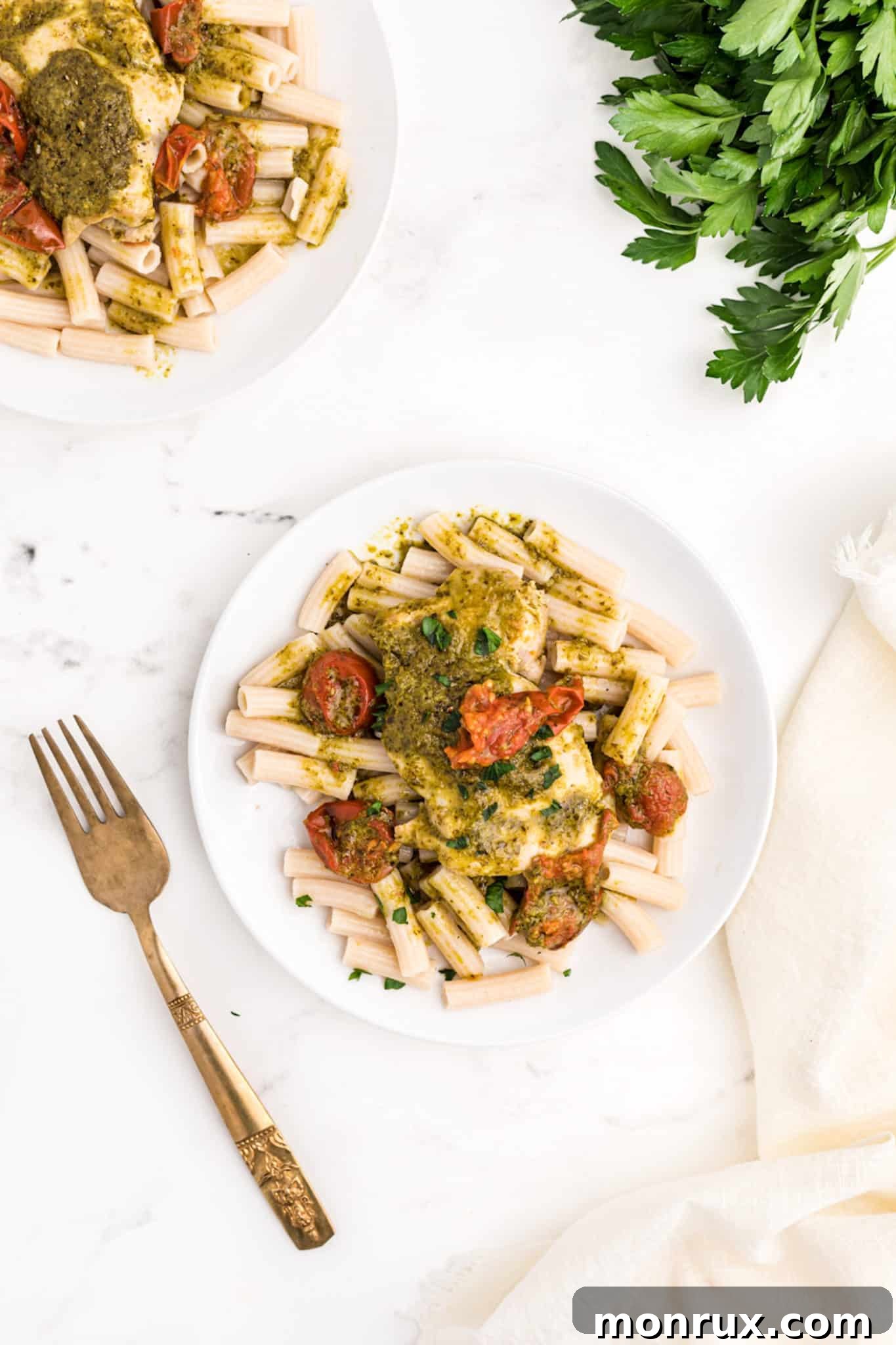 Two plates of pesto chicken served on top of gluten-free pasta with fresh basil.