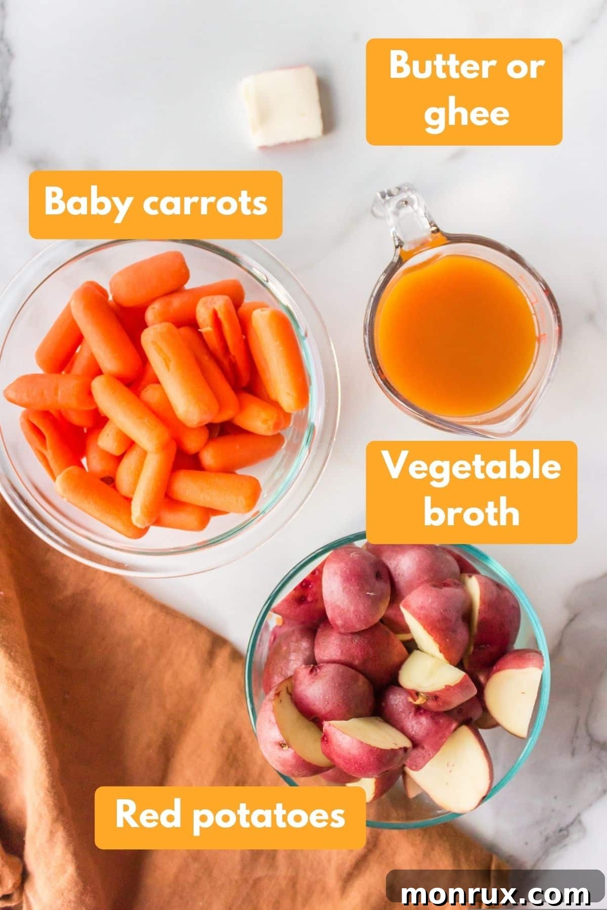 A flat lay image showcasing the simple ingredients required for Instant Pot Carrots and Potatoes: red potatoes, baby carrots, a stick of butter, and vegetable broth.