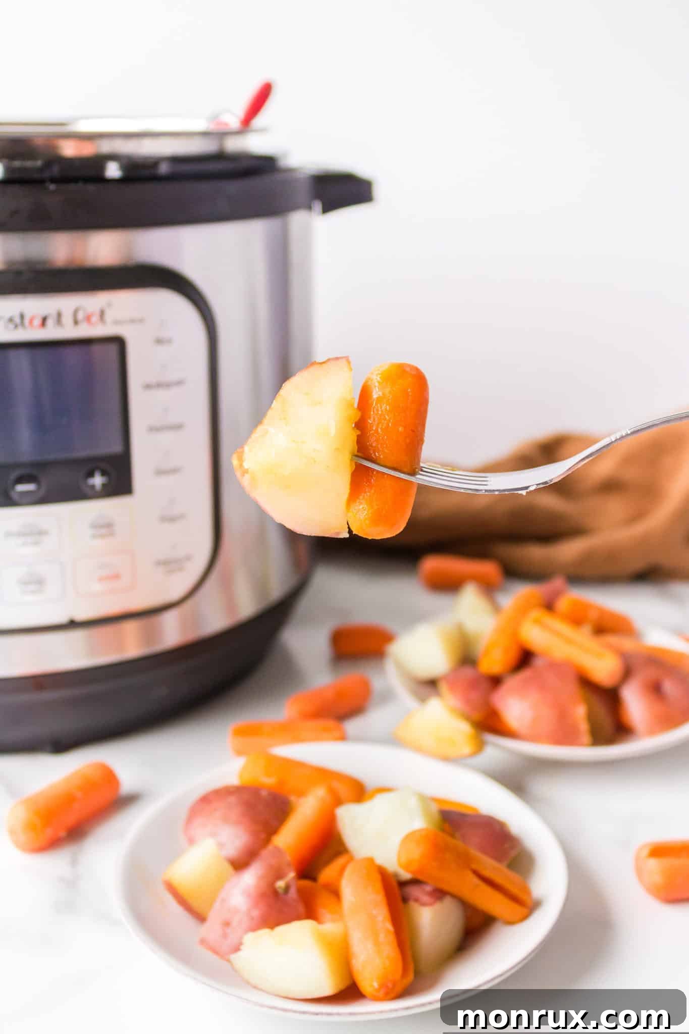 A close-up shot of a fork taking a bite of tender instant pot potatoes and carrots from a white plate.