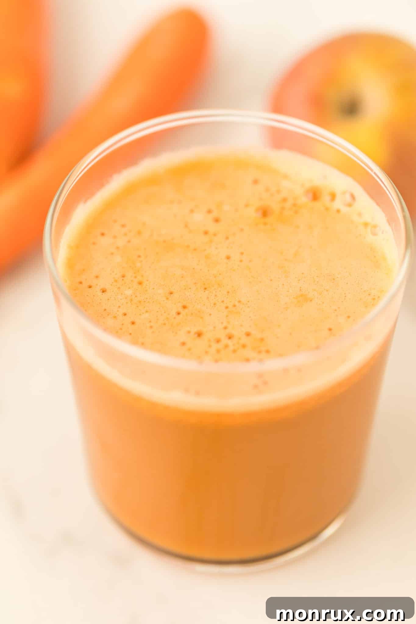 Freshly made carrot and cucumber juice in a beautiful glass on a table, garnished with a slice of cucumber.