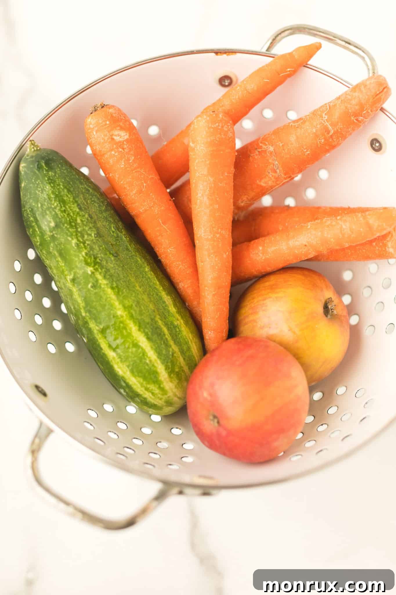Fresh carrots, cucumber, and an apple in a colander, washed and ready for juicing.