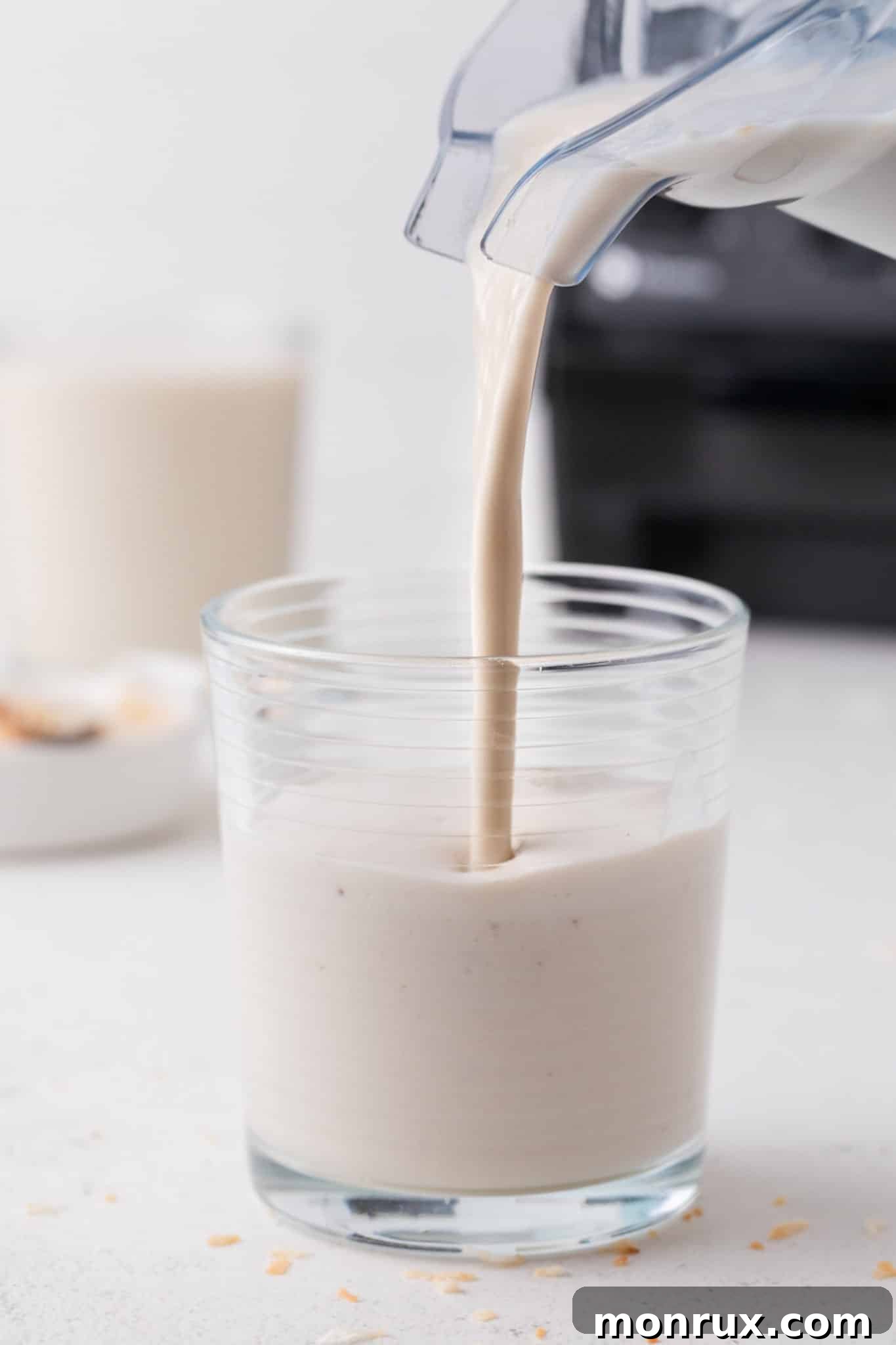 A delicious coconut shake being poured from a blender into a tall glass, ready to be served.