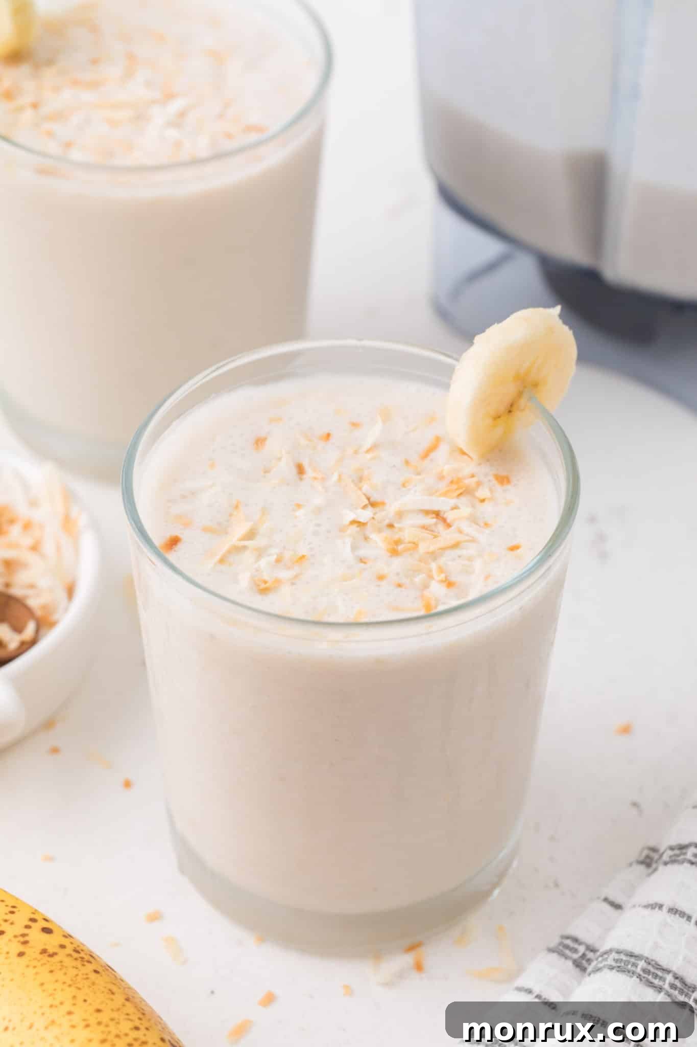 Two glasses filled with creamy coconut shake, garnished with toasted coconut flakes.