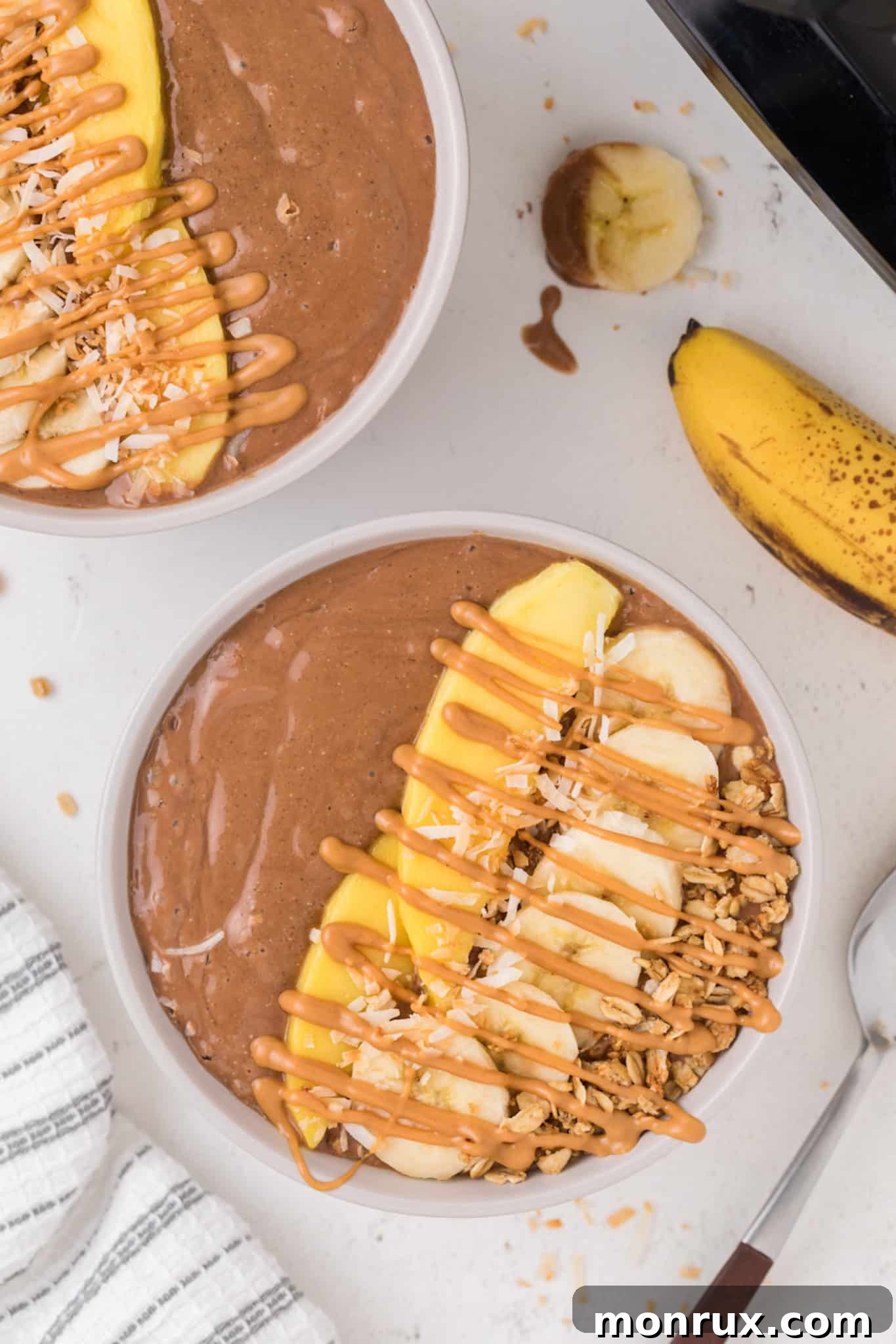 Two chocolate smoothie bowls artfully arranged with vibrant toppings like fresh mango slices, banana, and a sprinkle of seeds, ready to be enjoyed.