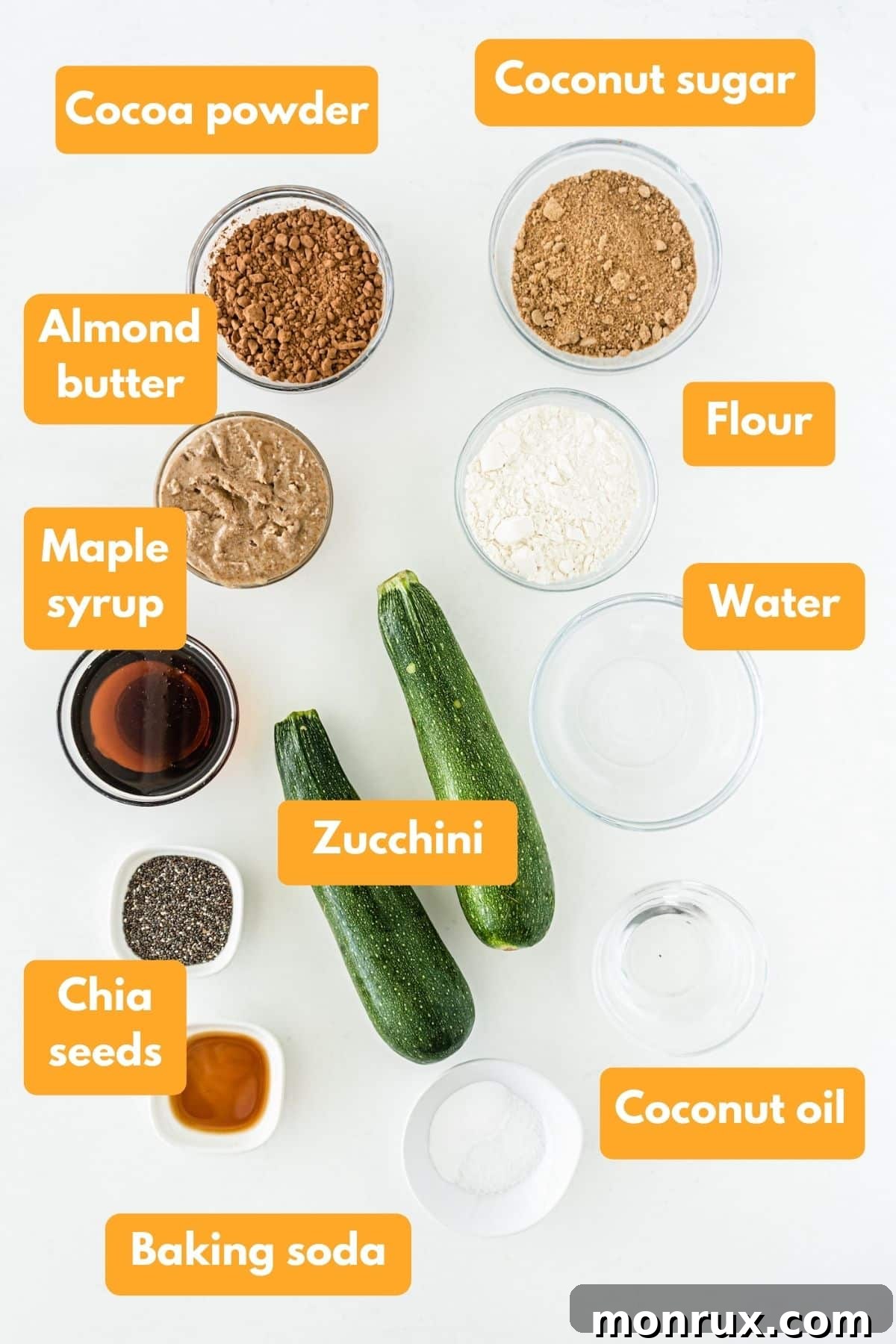 A selection of fresh ingredients laid out for making vegan zucchini brownies, including zucchini, almond butter, cocoa powder, and maple syrup.