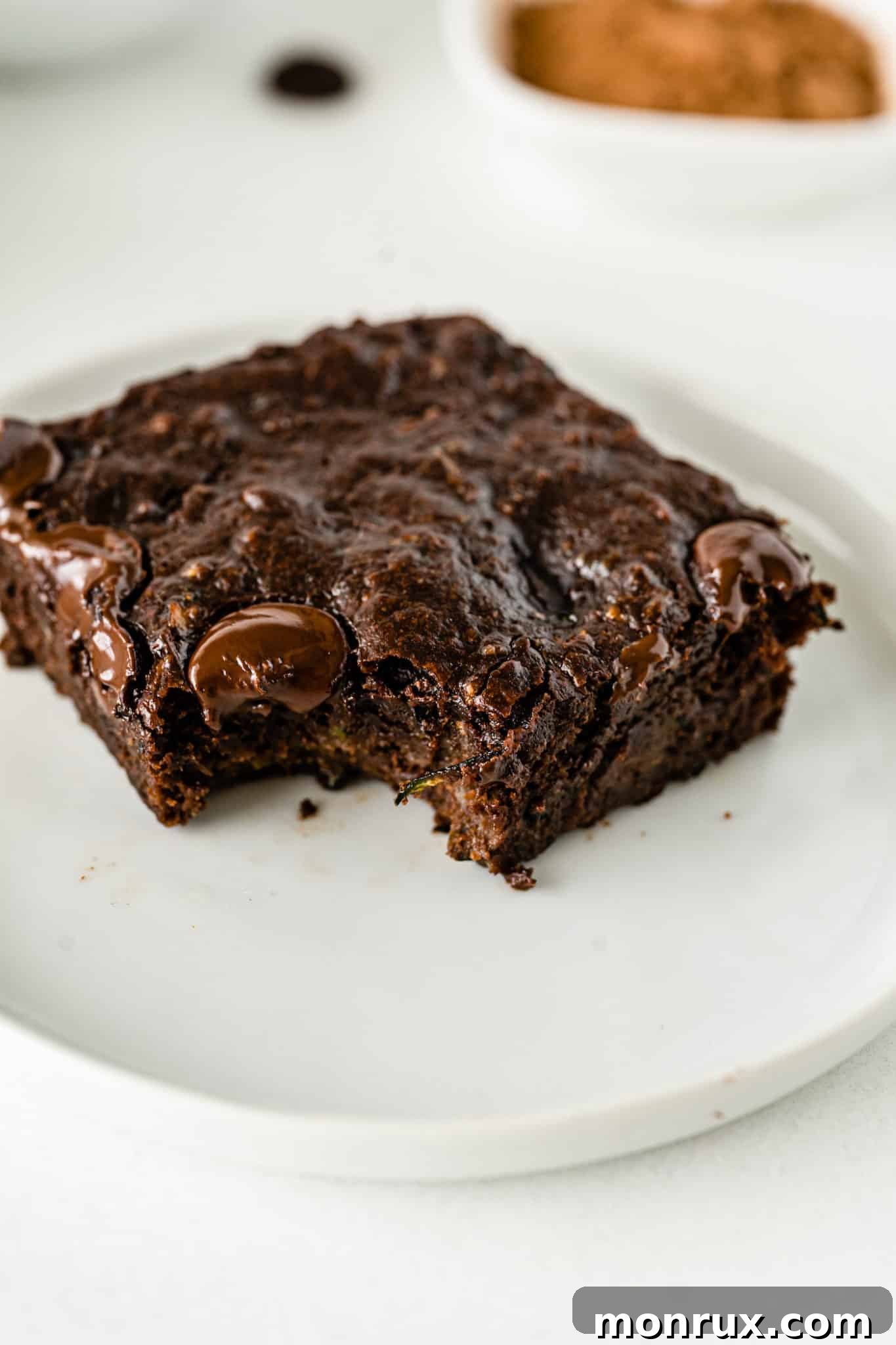 A square-cut vegan zucchini brownie served on a white plate, showcasing its fudgy interior.