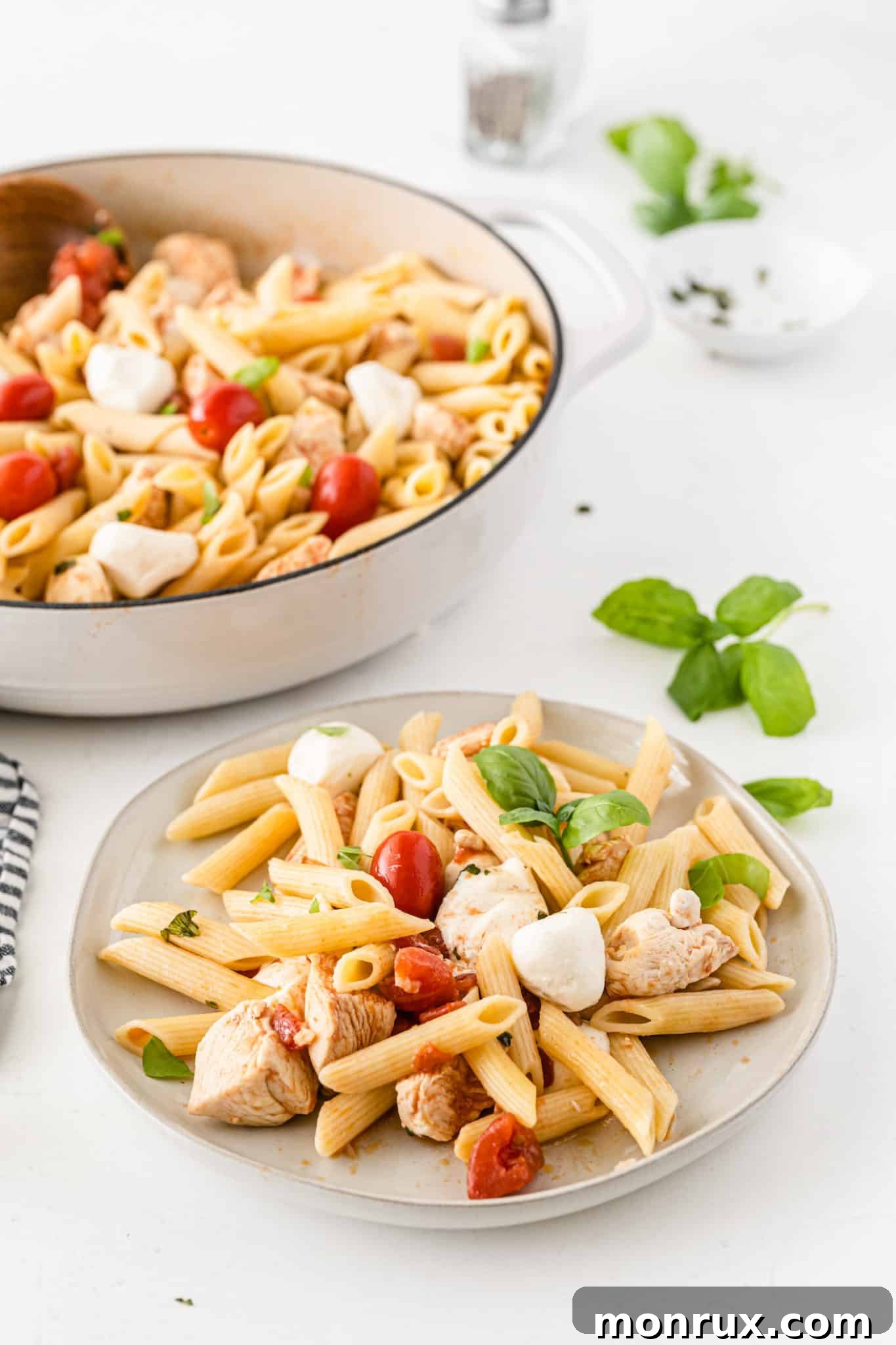 A serving of tomato basil pasta on a white plate, garnished with fresh basil leaves.