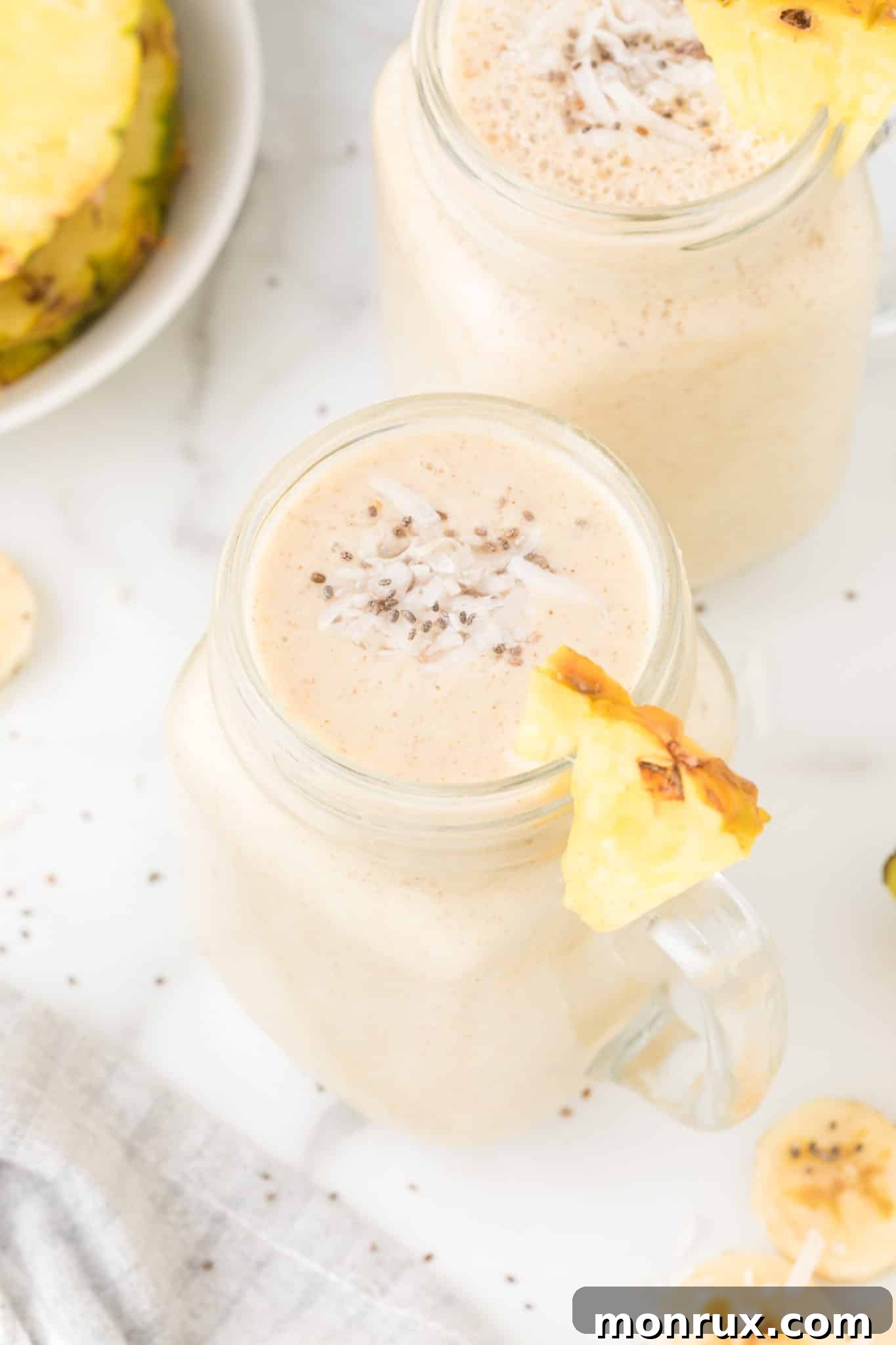 Two glasses of vibrant pineapple banana smoothies, garnished with fresh pineapple wedges and mint leaves, ready to be enjoyed.
