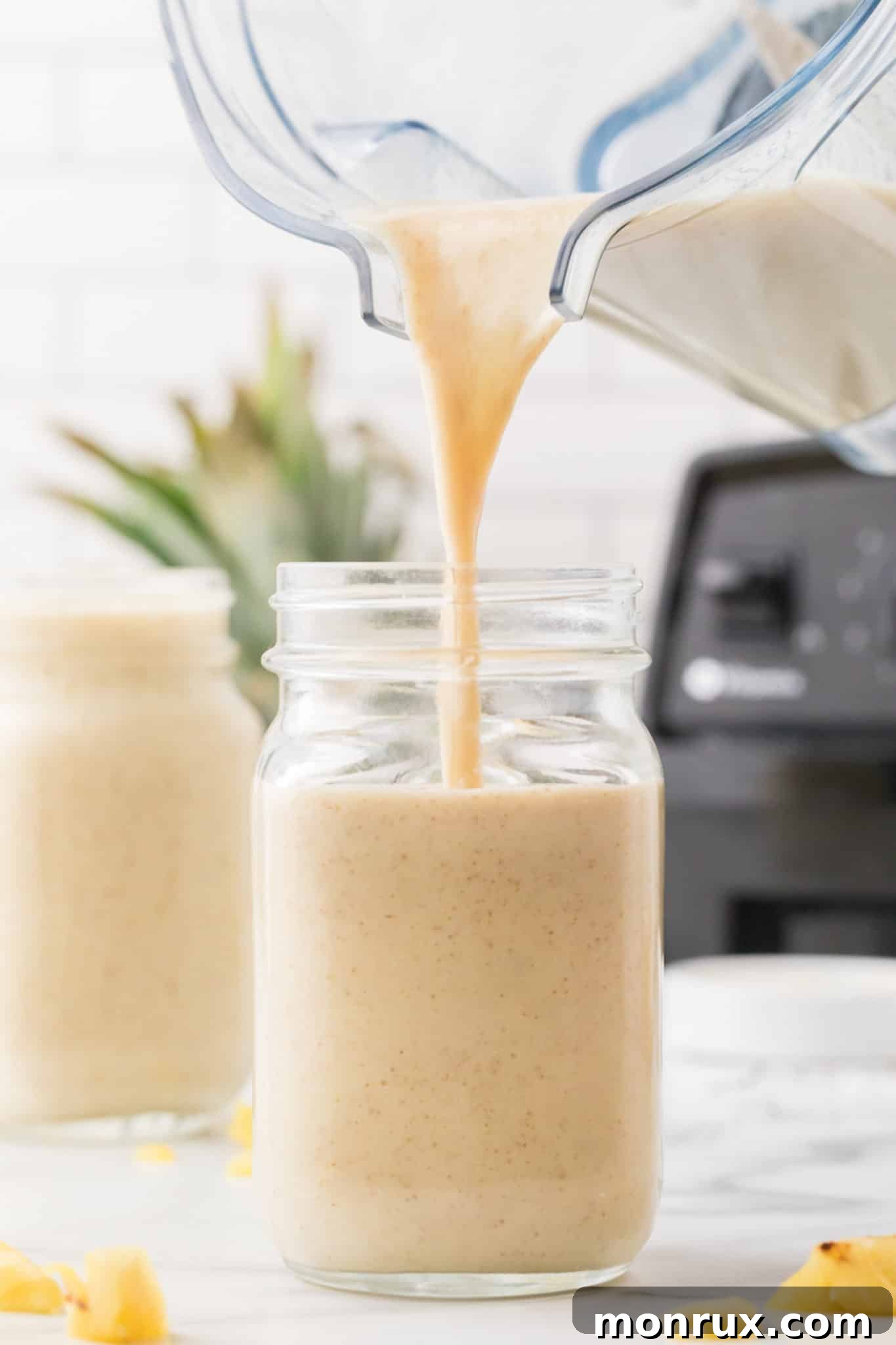 A creamy pineapple banana smoothie being poured from a blender into a tall glass, showcasing its smooth texture.