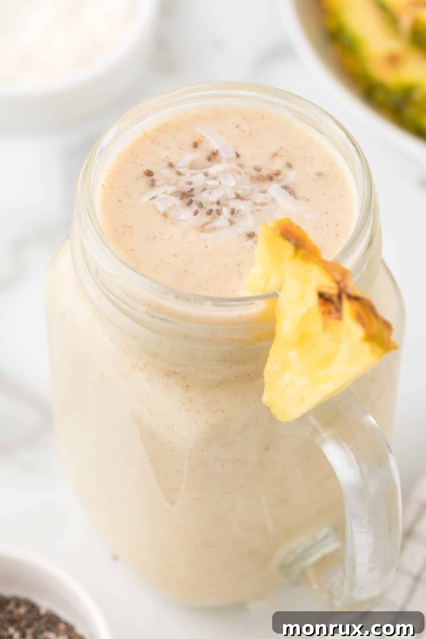 A single glass of a vibrant pineapple banana smoothie, garnished with a fresh pineapple wedge, set against a bright, clean background.
