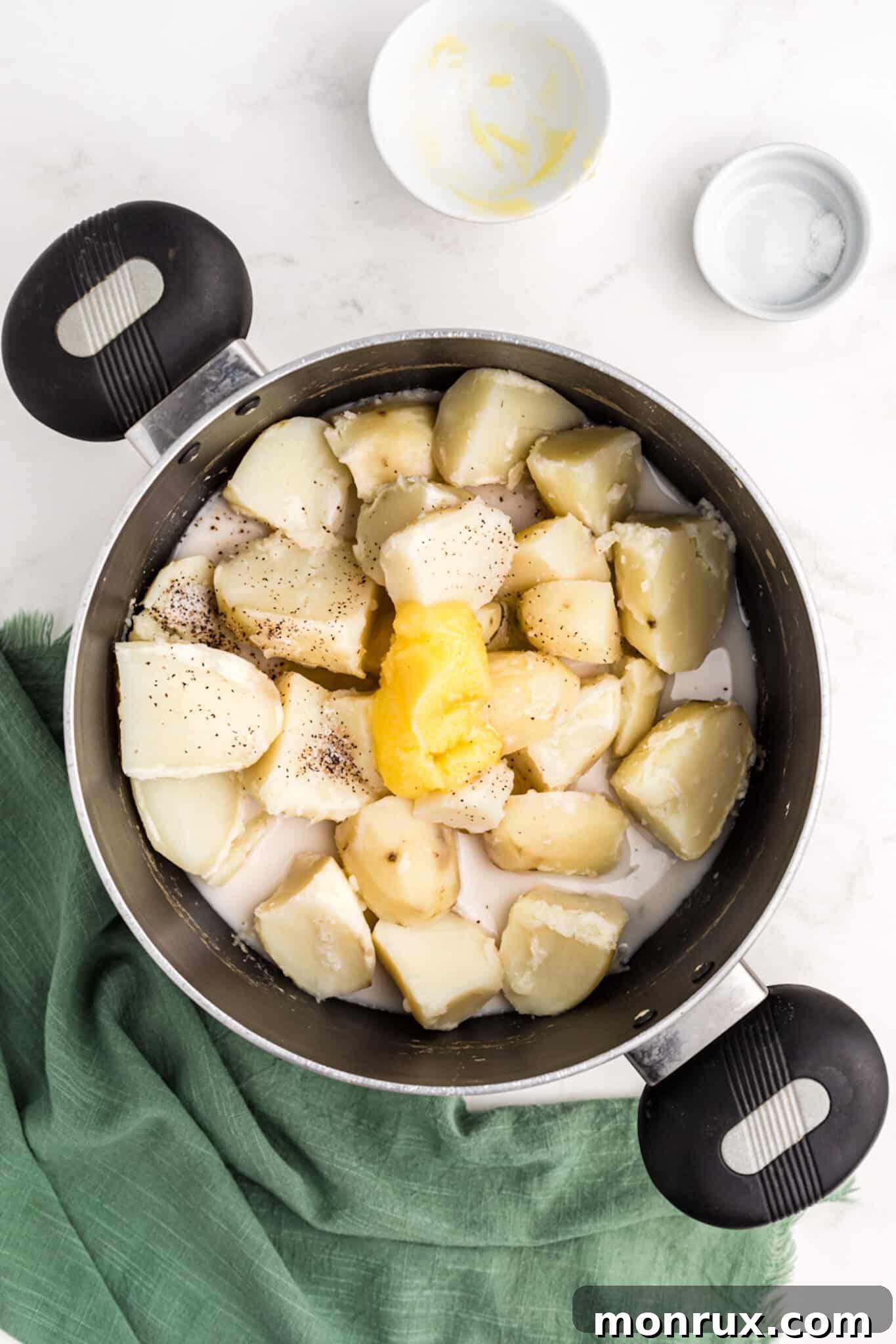 Ghee, almond milk, and seasonings being added to drained potatoes in a pot.