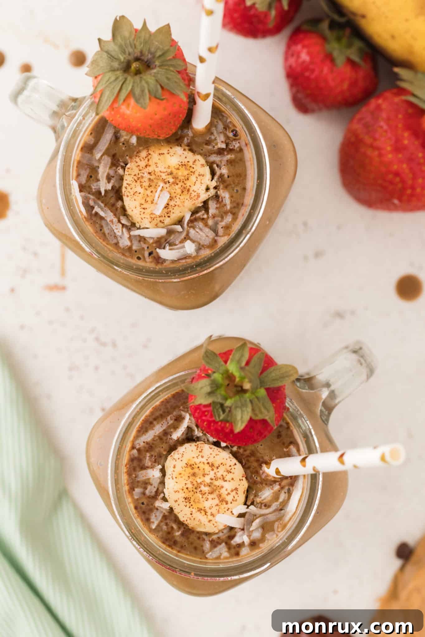 Two glasses of rich chocolate smoothie, garnished with fresh fruit and shredded coconut, perfect for a high-calorie treat.