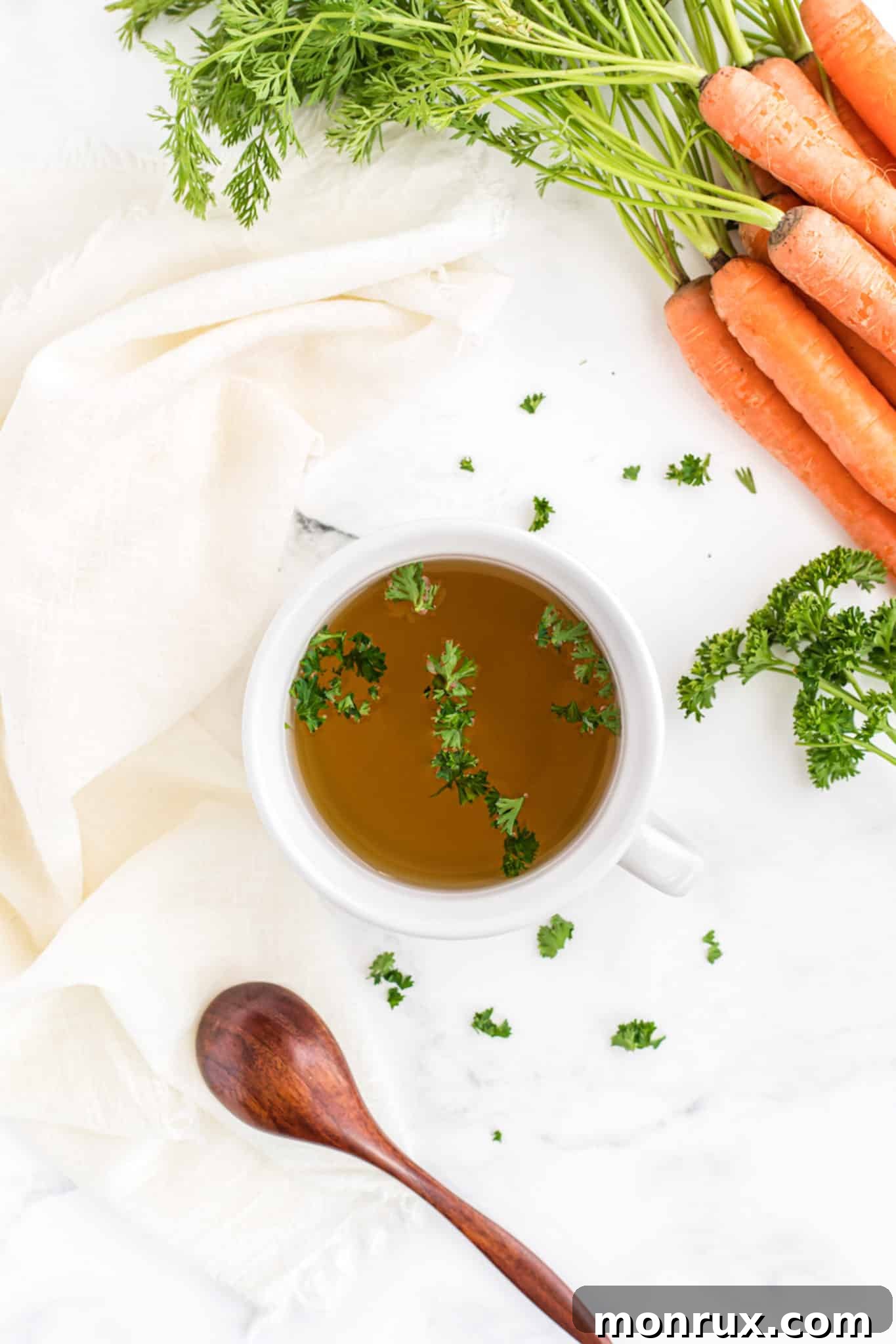 bowl of vegetable broth on a table with fresh carrots.