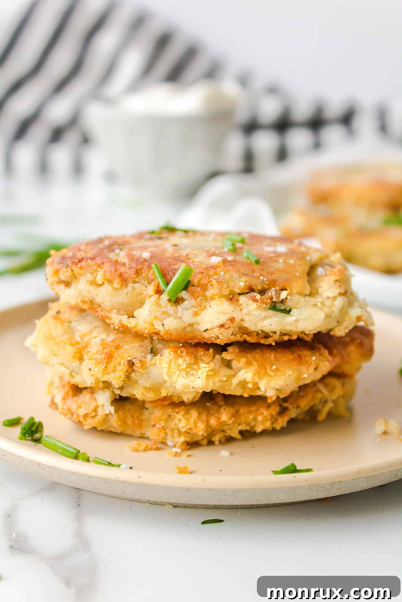 A stack of golden brown mashed potato fritters, garnished with fresh green chives, ready to be served.