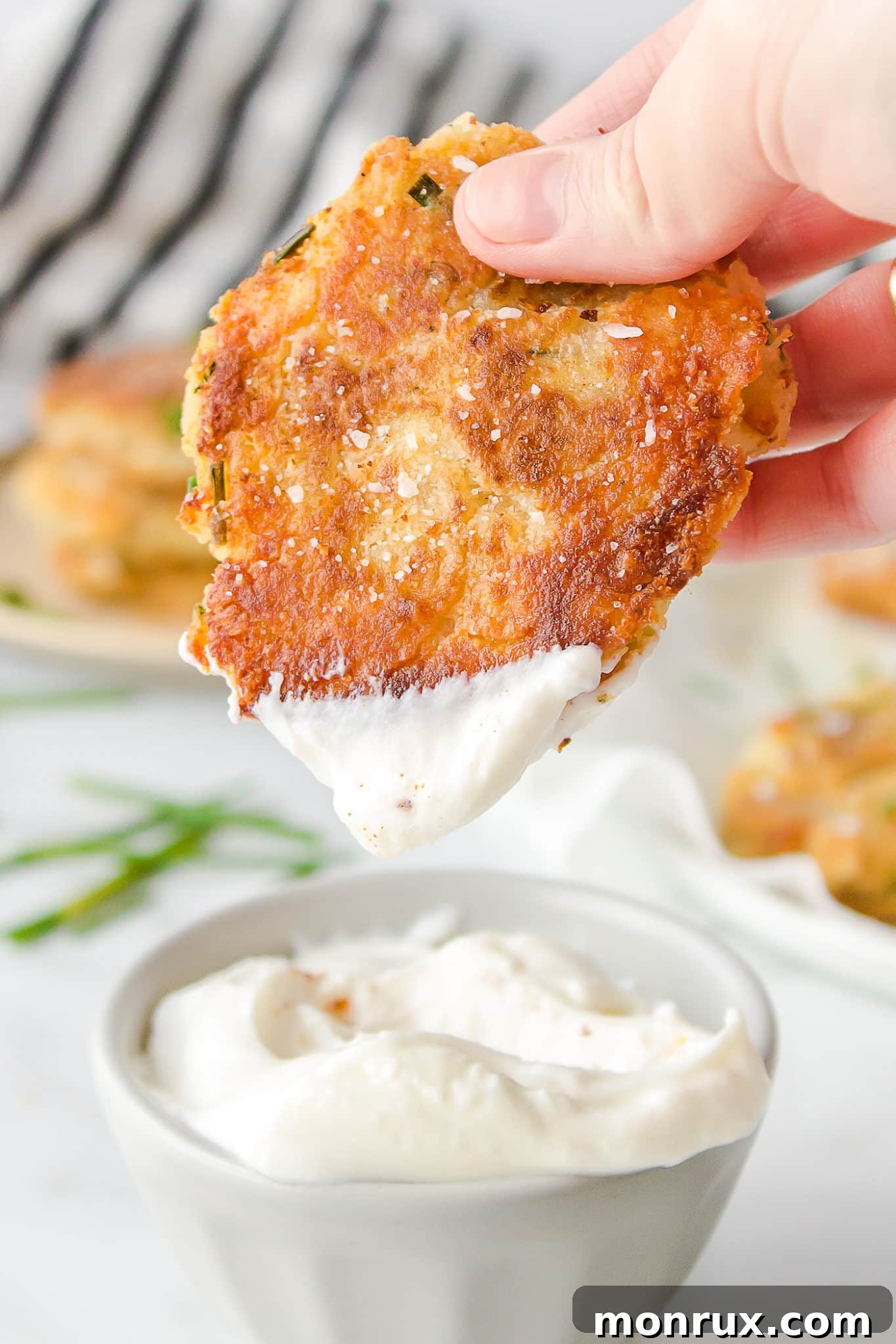 A crispy mashed potato fritter being dipped into a creamy white sauce, highlighting its golden texture.