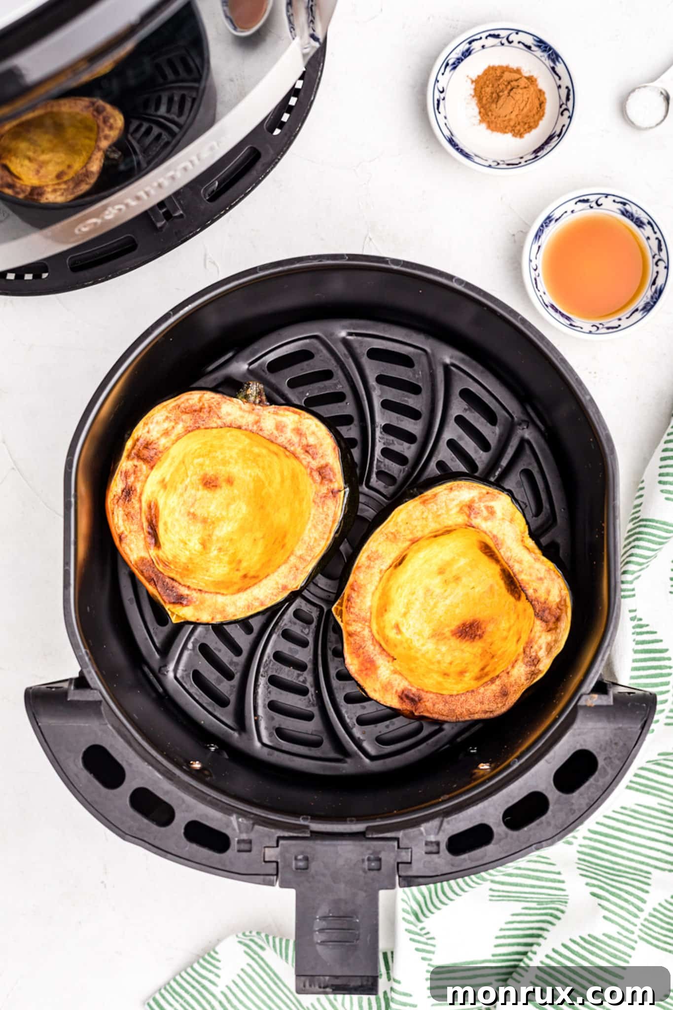 Two halves of perfectly roasted acorn squash in an air fryer basket, ready to be served, highlighting their golden-brown edges.