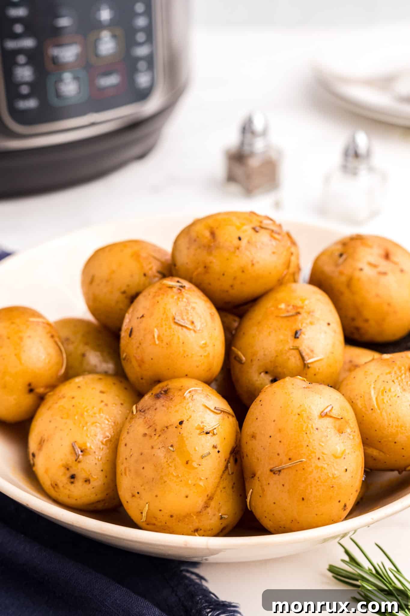 Cooked Instant Pot baby potatoes with garlic and rosemary on a plate, garnished with fresh rosemary.