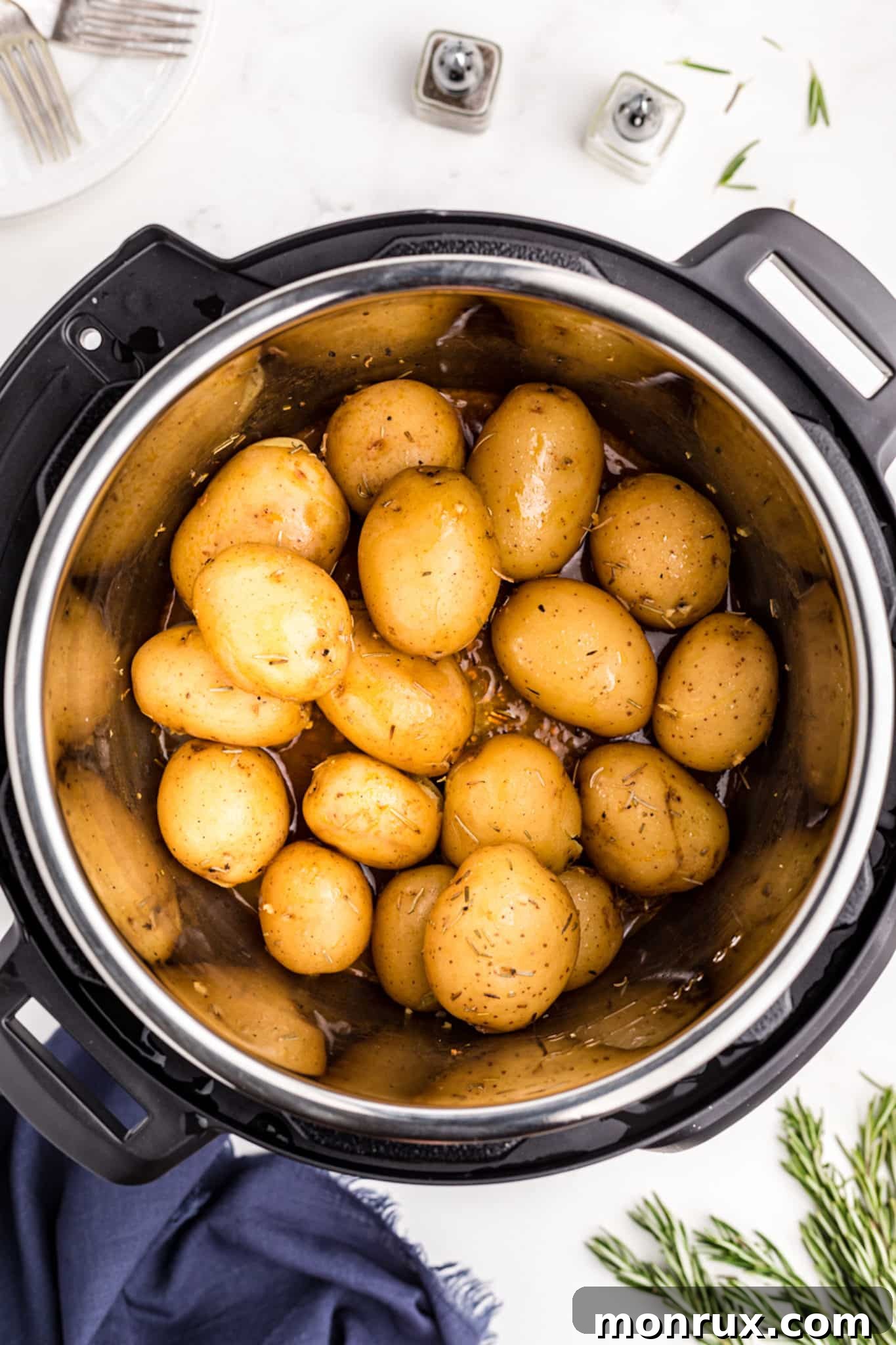Baby potatoes, minced garlic, and vegetable broth inside the Instant Pot before cooking.