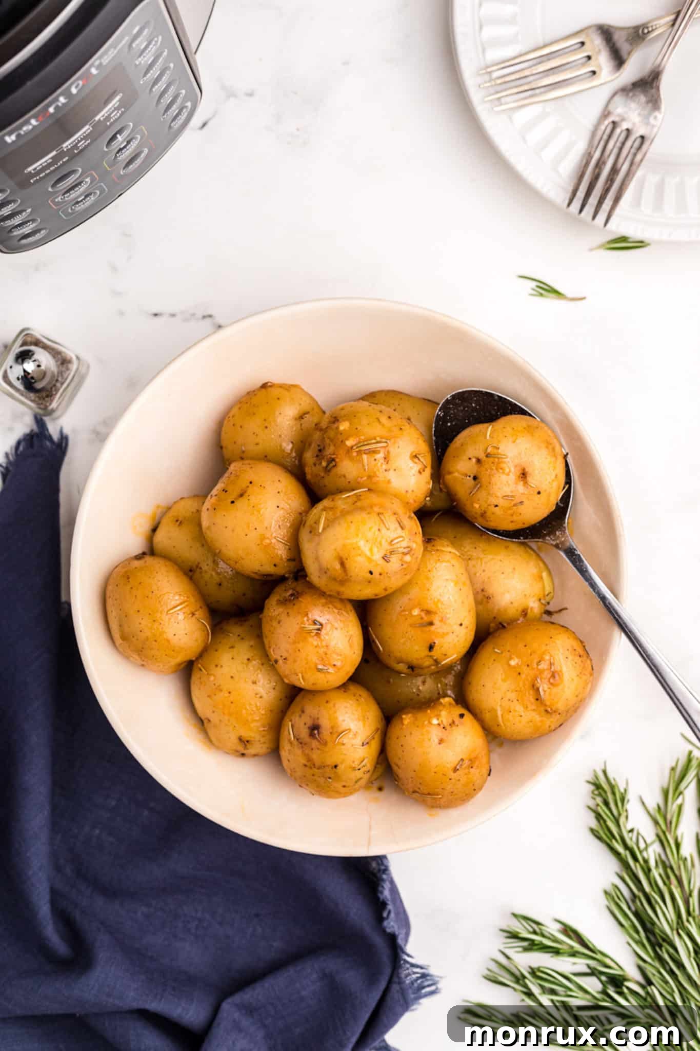 A bowl of cooked garlic and rosemary baby potatoes with a serving spoon, ready for the table.