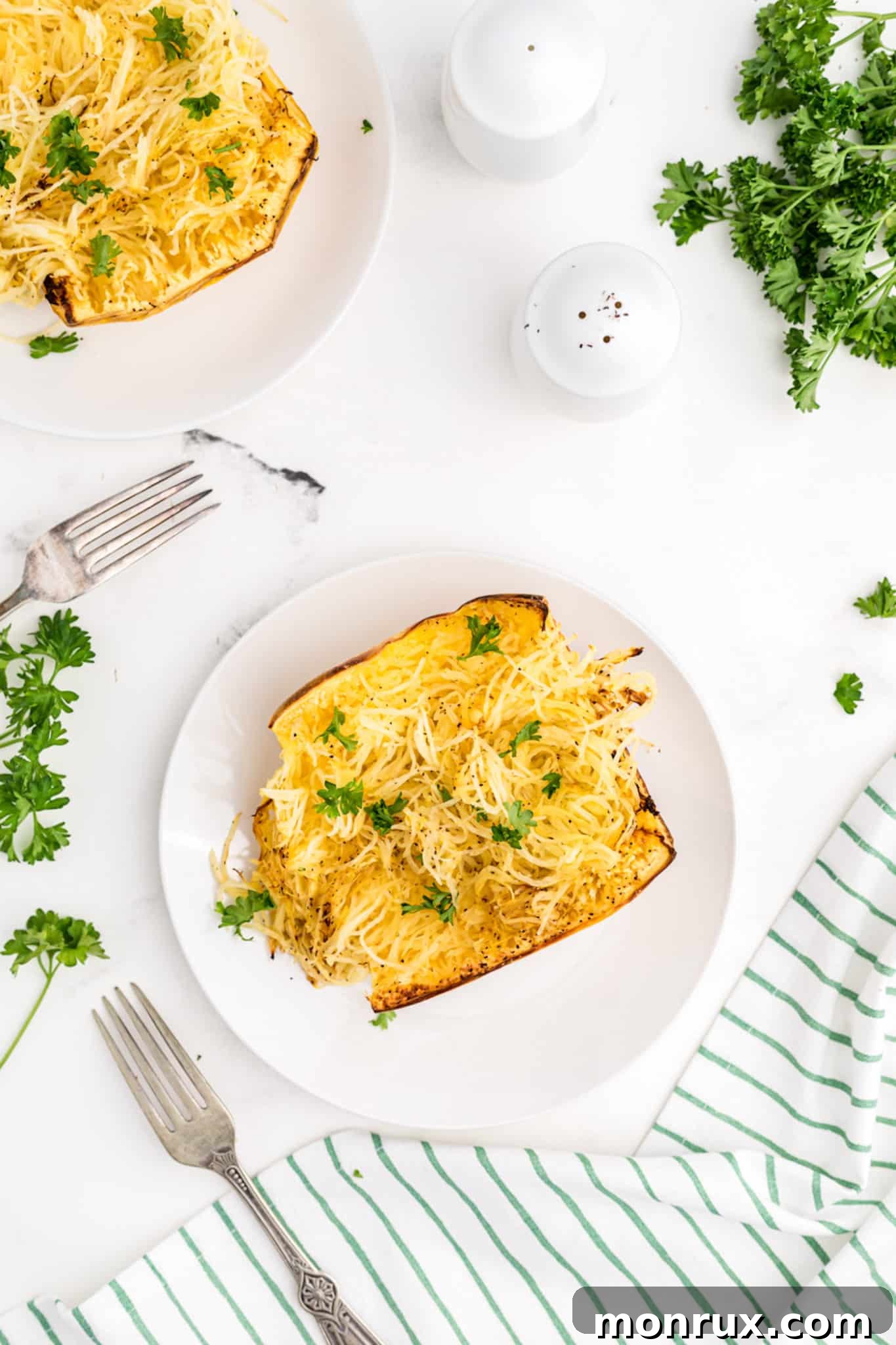 two plates of cooked spaghetti squash with parsley garnish.