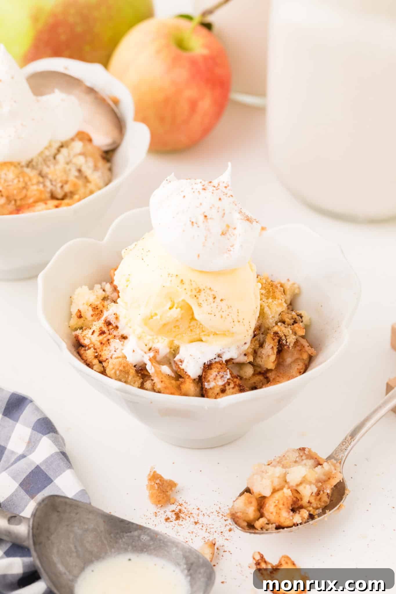 Two bowls of air fryer apple crisp topped with a scoop of vanilla ice cream and a dusting of cinnamon.
