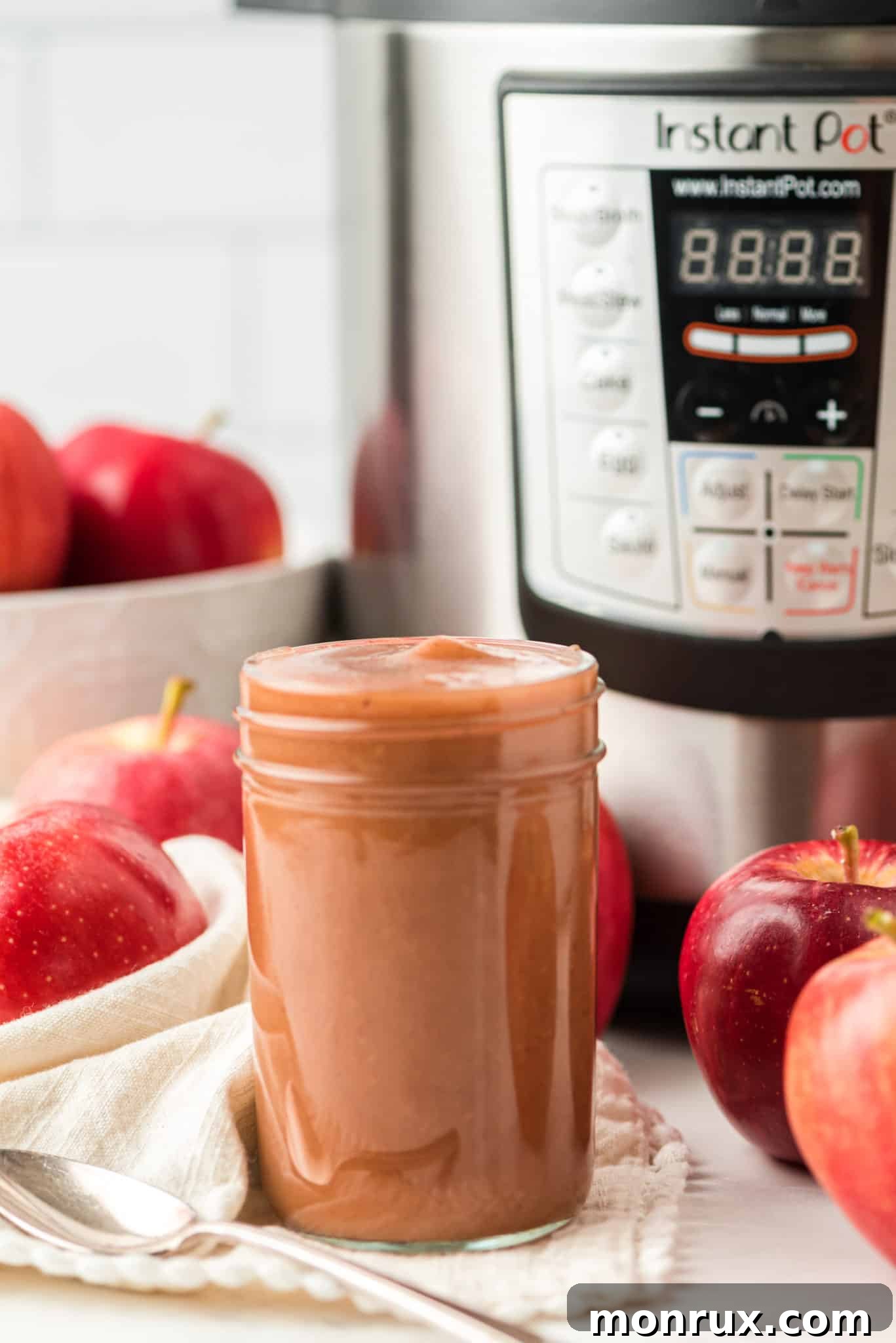 A jar of homemade Instant Pot apple butter in front of an Instant Pot pressure cooker.