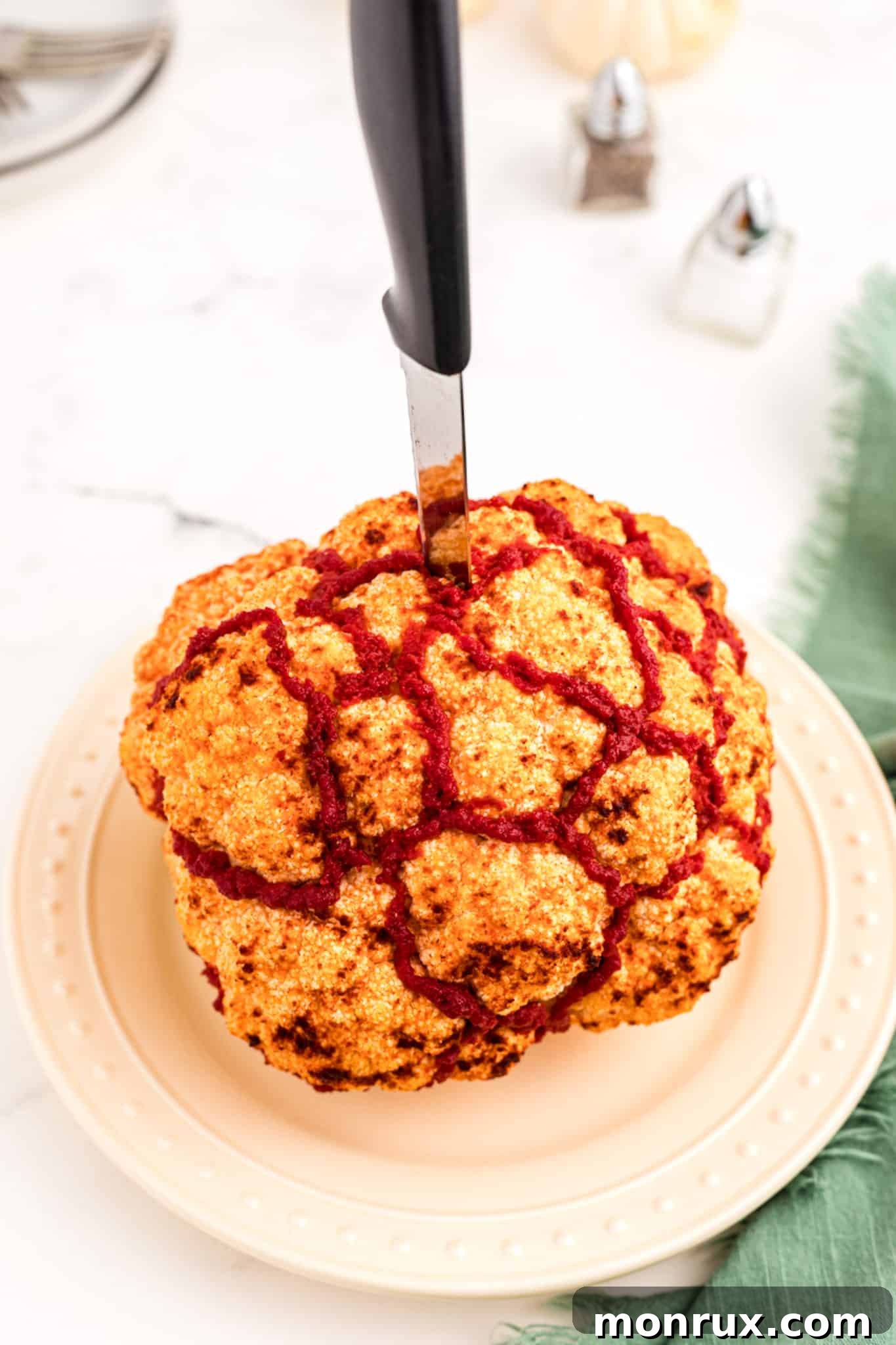 A perfectly roasted whole cauliflower, expertly styled to resemble a human brain, pierced dramatically with a knife, ready for a Halloween feast.