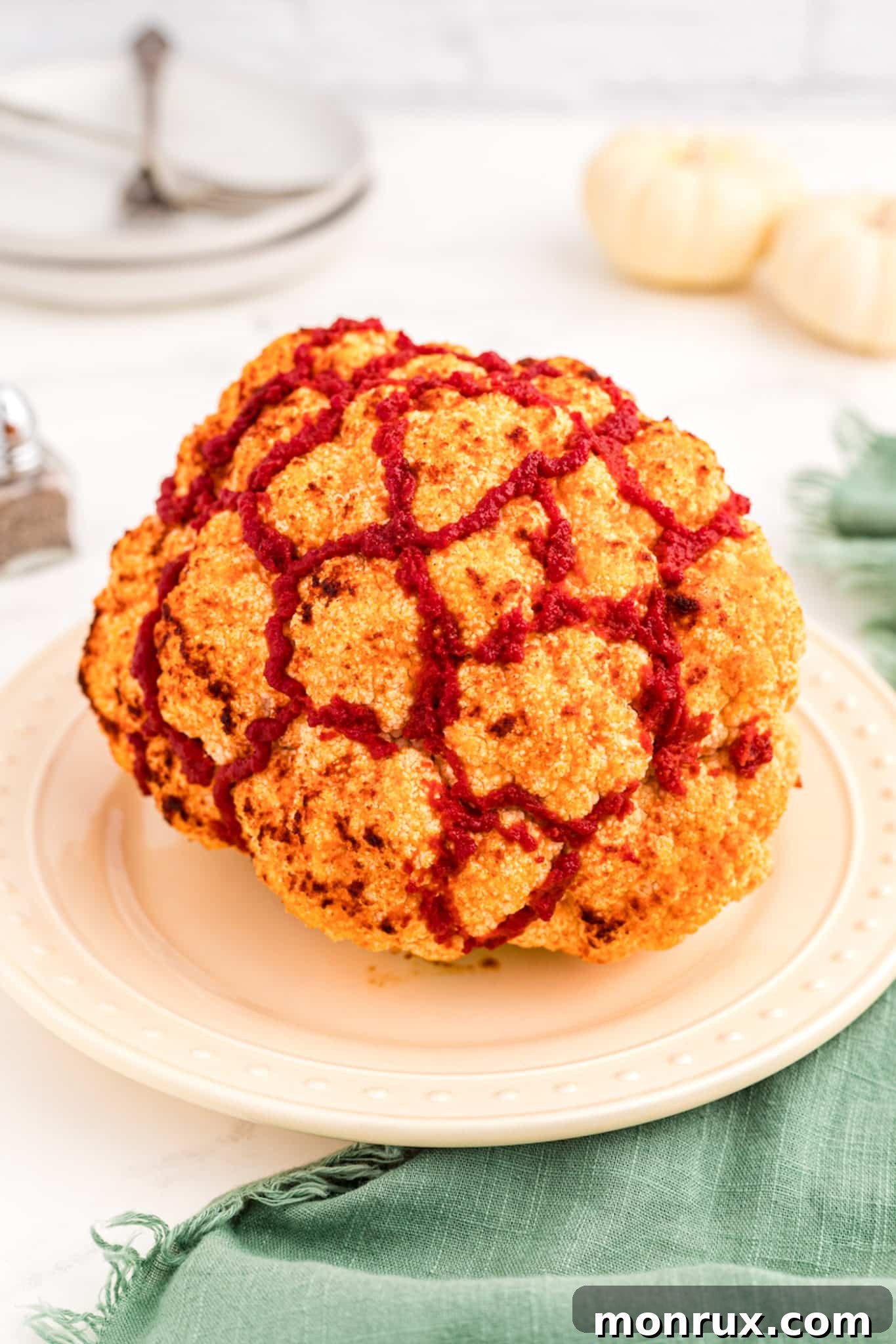 A perfectly cooked whole roasted cauliflower brain, presented on a dark plate with a dramatic knife piercing, ready to serve as a Halloween centerpiece.