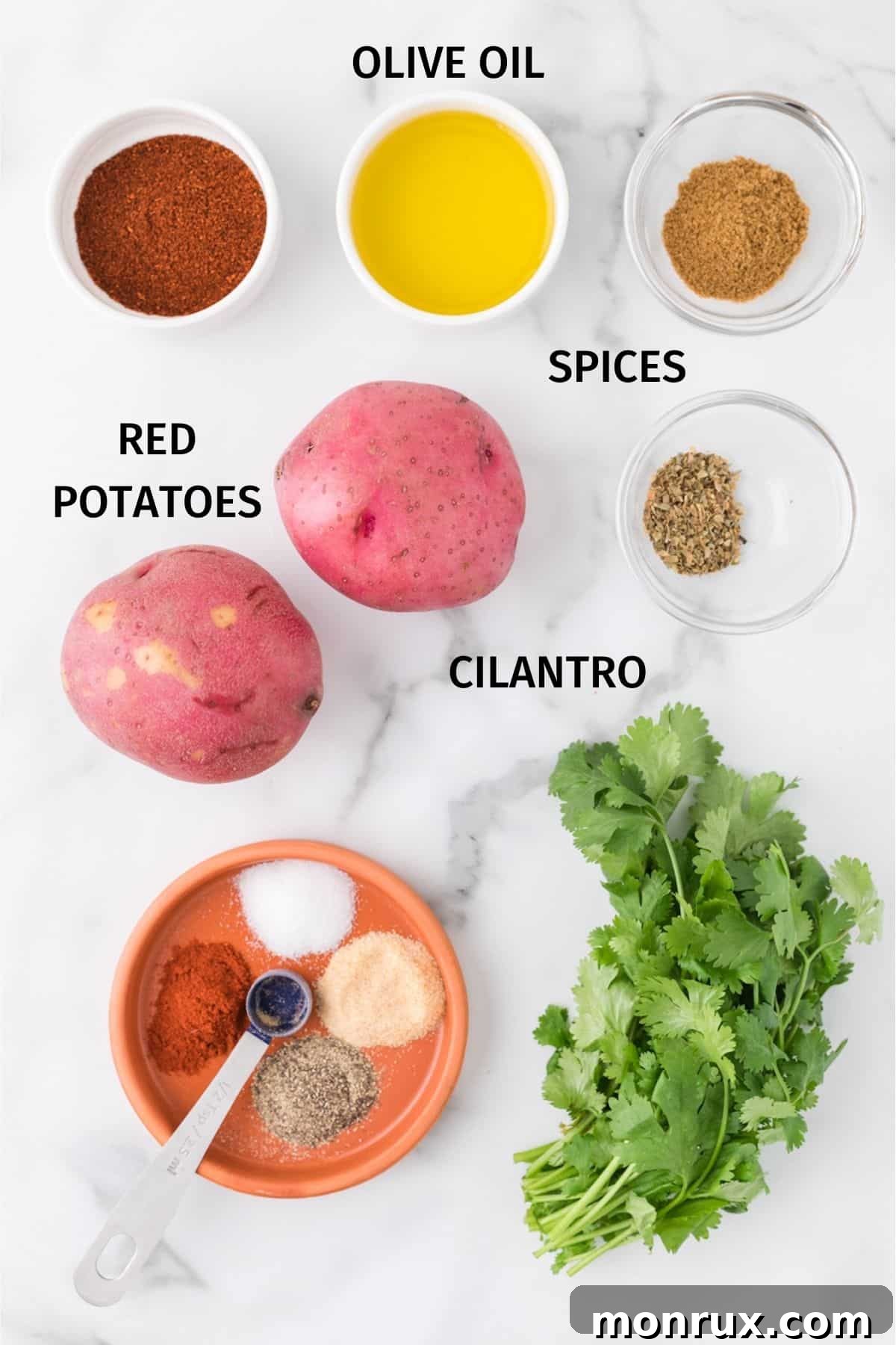 A flat lay of fresh ingredients for making Mexican potatoes, including red potatoes, olive oil, and a selection of dried spices.