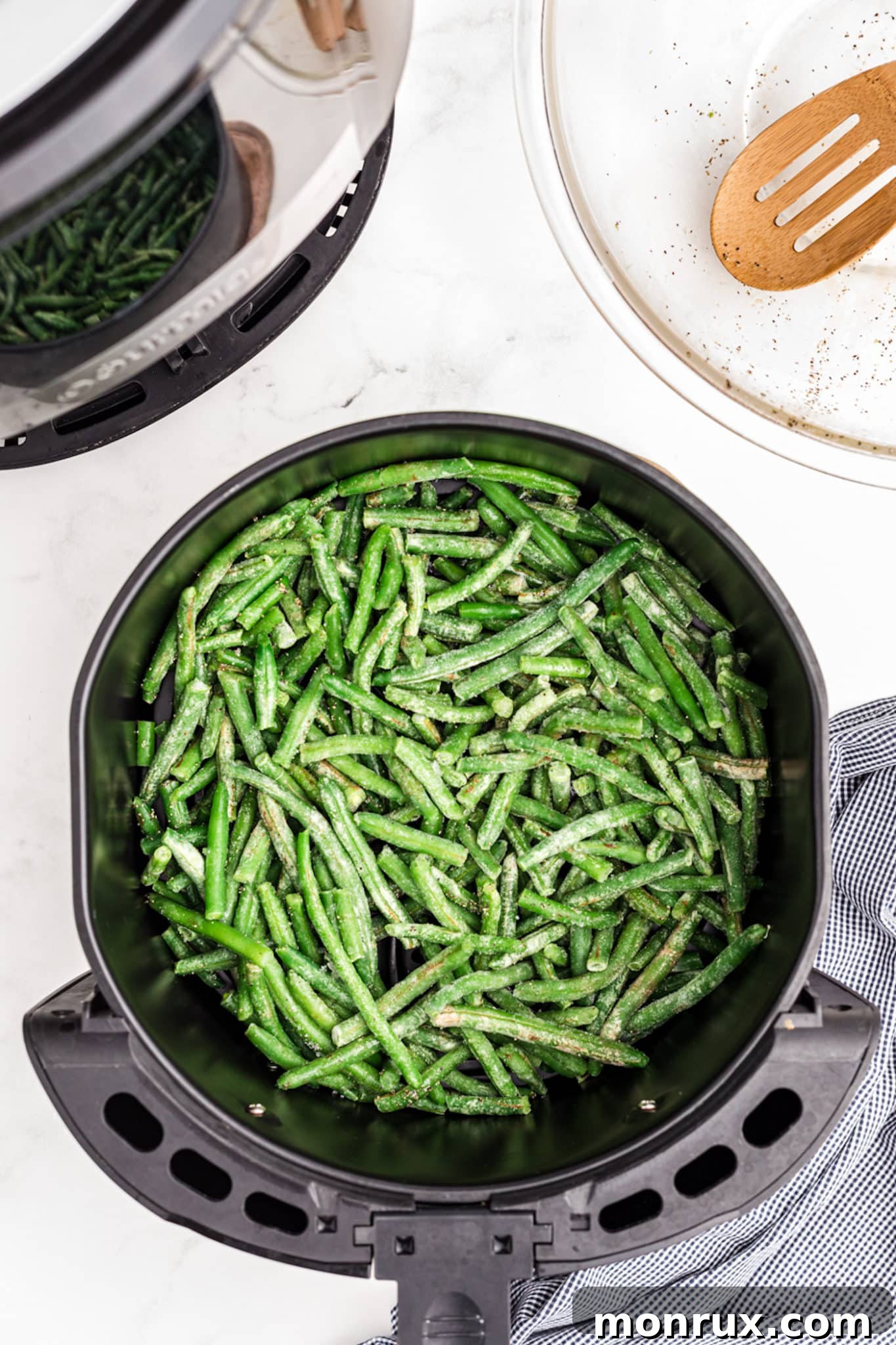 Frozen green beans spread out in an air fryer basket, ready for cooking.