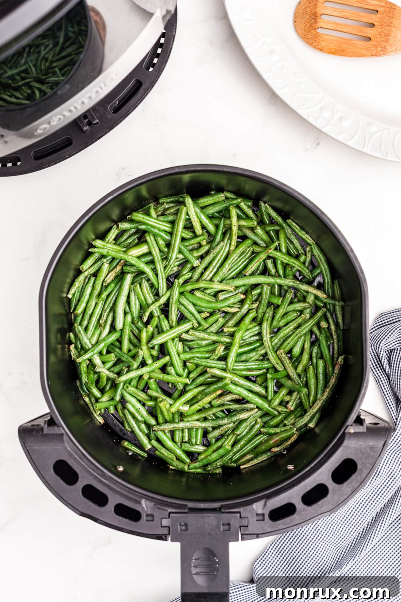 Cooked green beans visible in the air fryer basket after the initial cooking phase, showing signs of crisping.