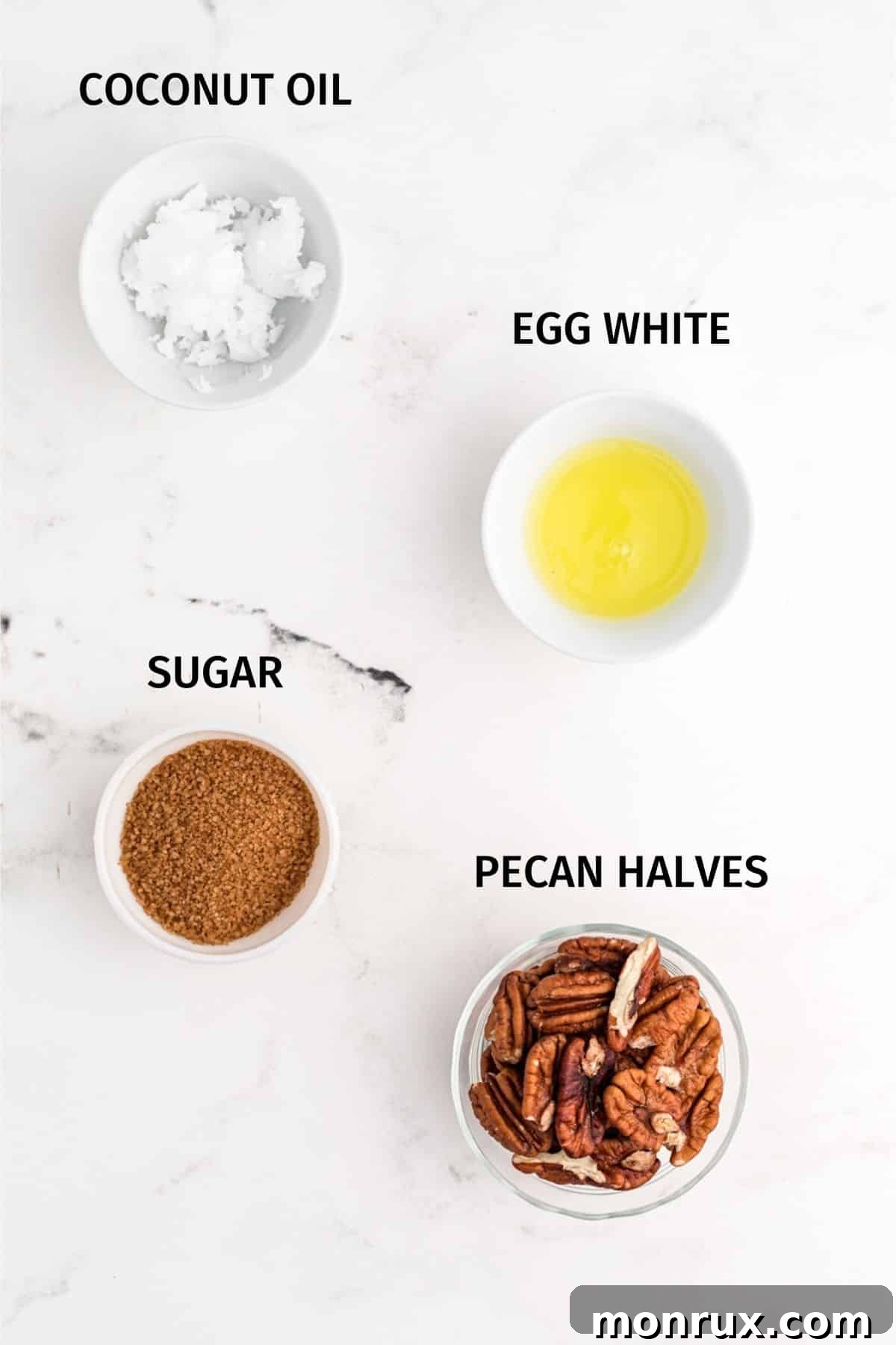 Essential ingredients for air fryer candied pecans laid out on a kitchen counter: raw pecan halves, coconut oil, an egg white, and granulated sugar.
