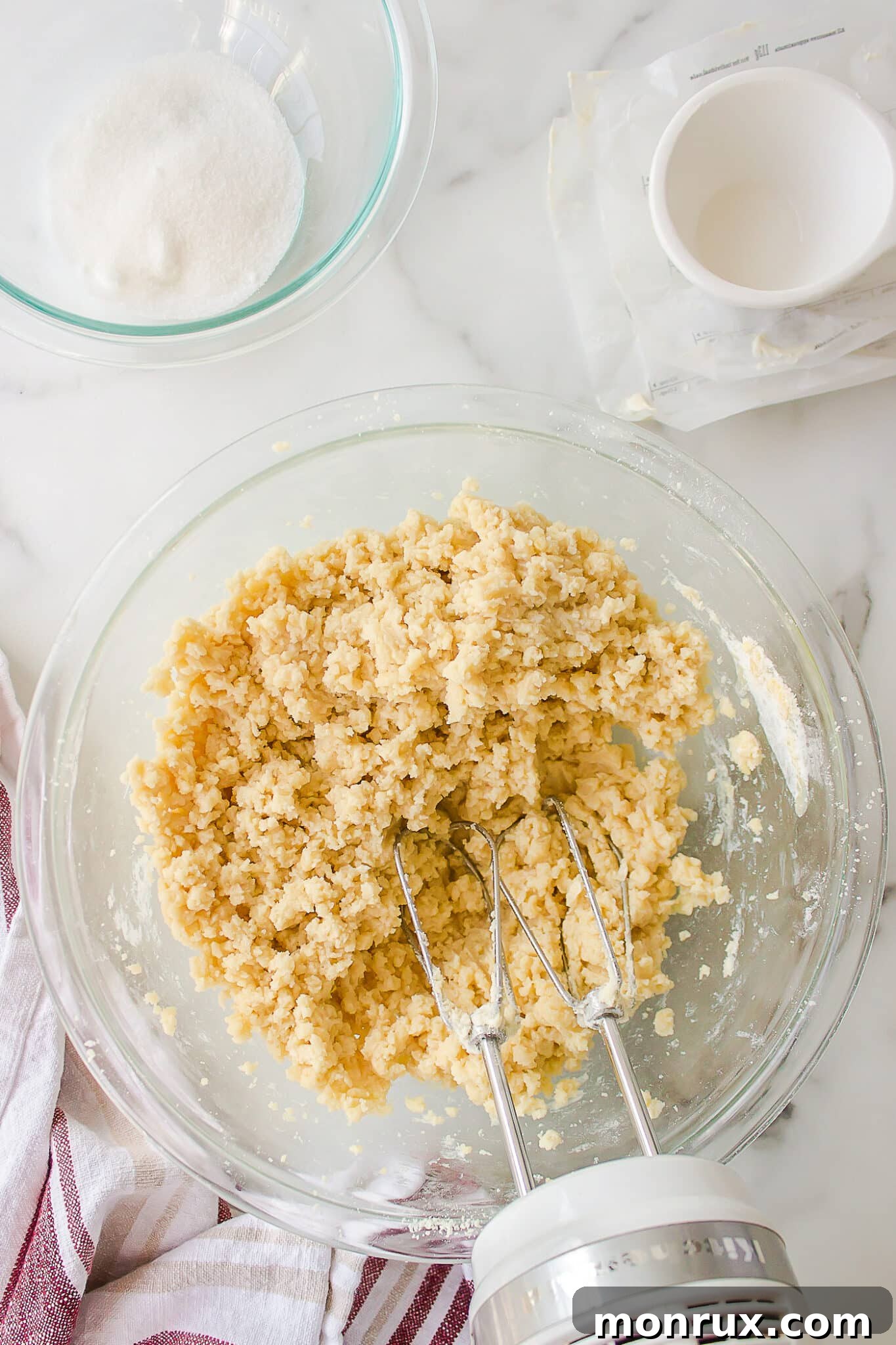 Mixing together wet and dry ingredients to form sugar cookie dough using a hand mixer.
