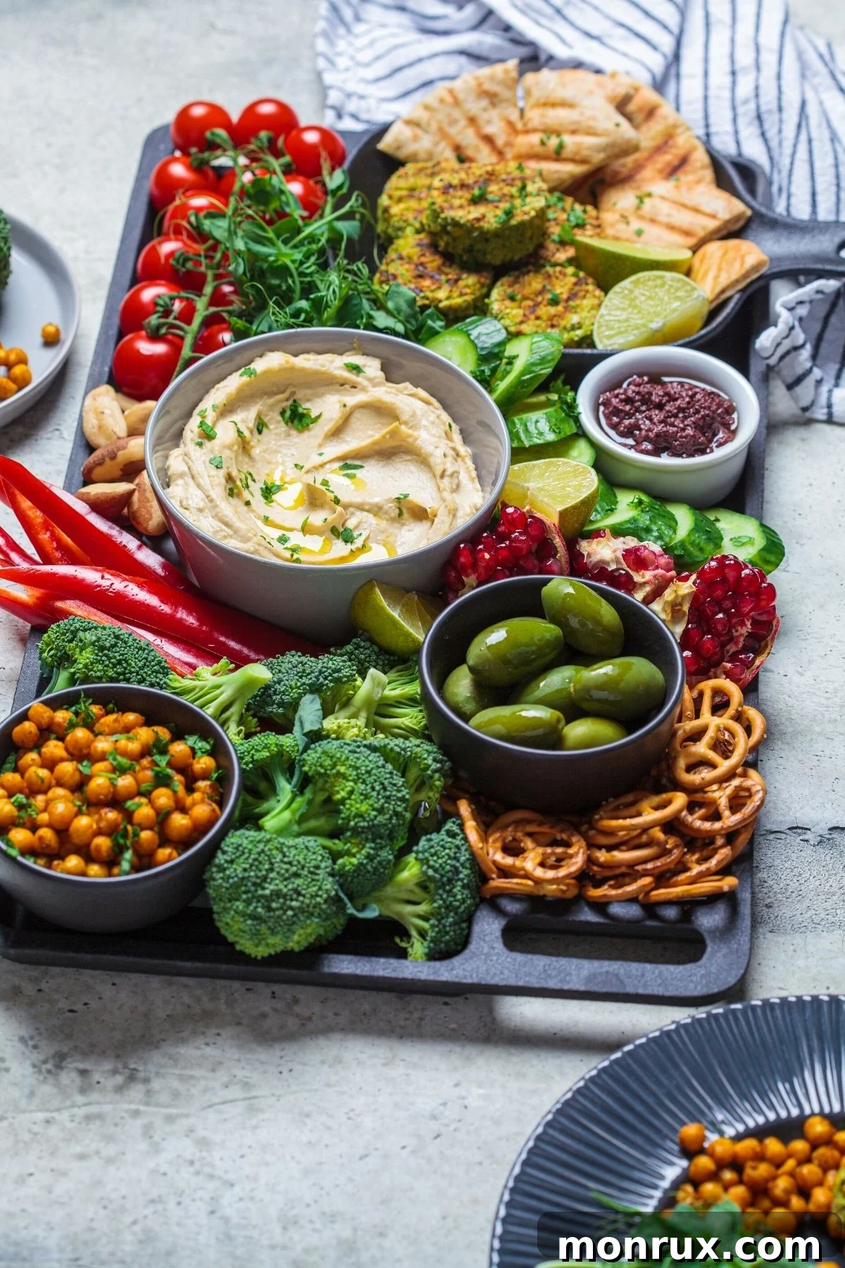 A beautifully arranged vegan charcuterie board featuring an array of fresh vegetables, a bowl of creamy hummus, and various crackers, perfect for healthy snacking.