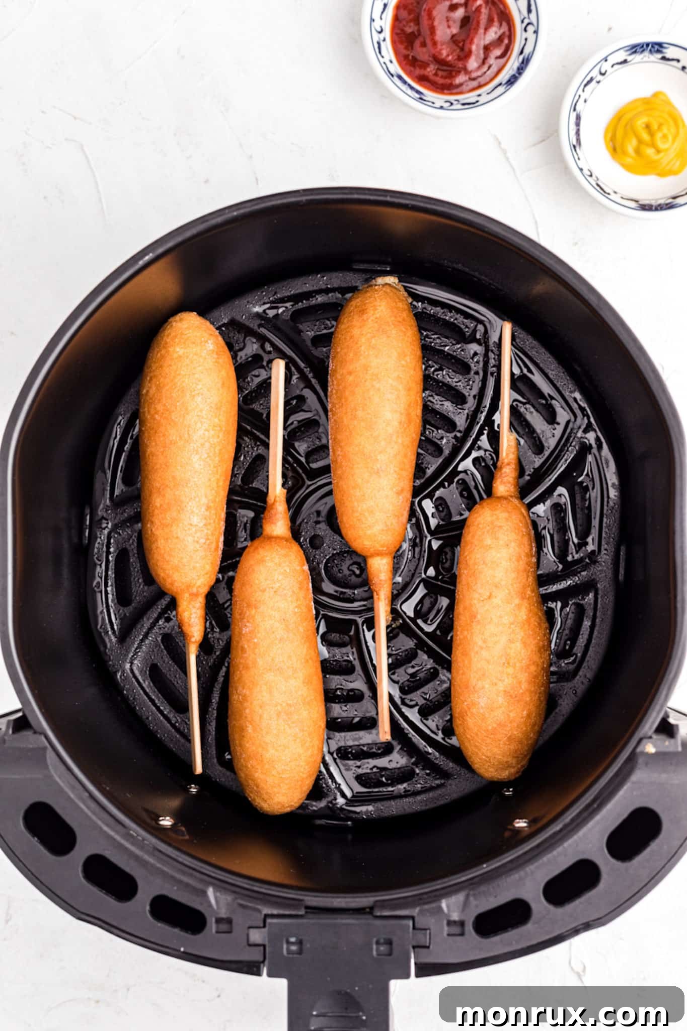 An air fryer basket containing several frozen corn dogs arranged in a single layer.