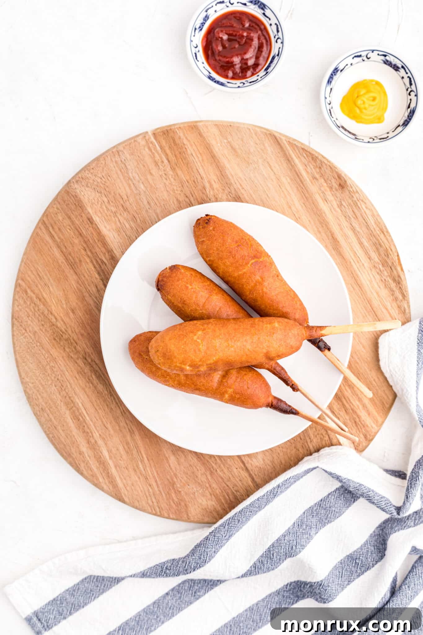 A plate featuring freshly air-fried corn dogs, garnished with a side of ketchup and mustard.